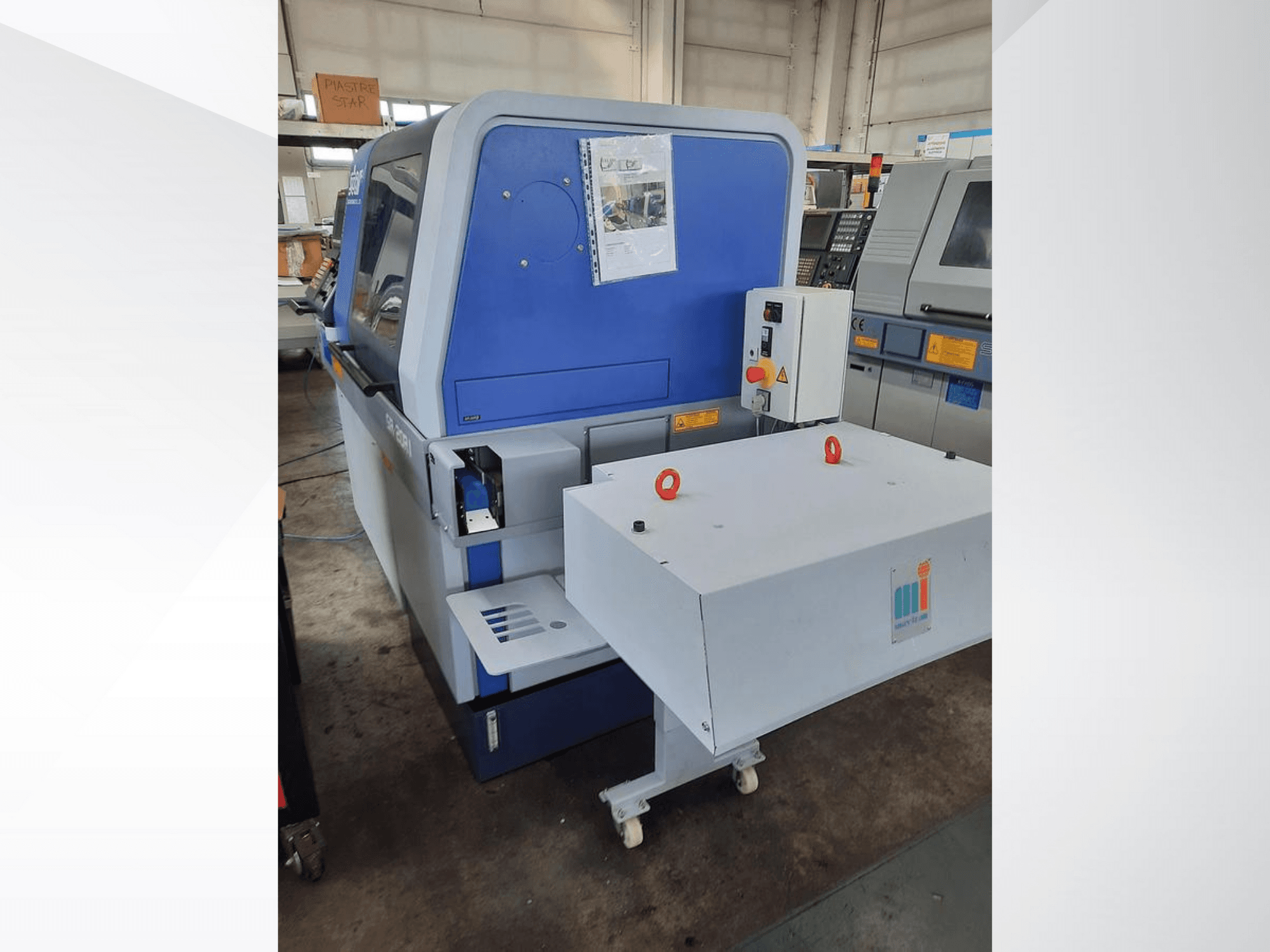 Beyaz konveyörlü mavi endüstriyel makine, kontrol panelini ve ekli güvenlik özelliklerini gösterir, yandan görünüm.