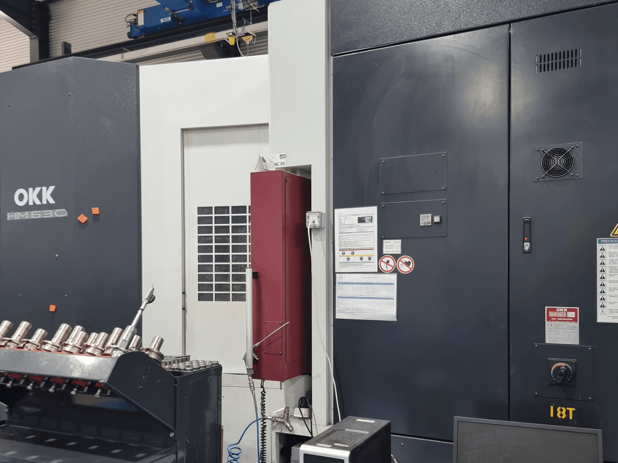 OKK HM630 yatay işleme merkezi; kontrol paneli, güvenlik uyarıları ve yan taraftaki takım saklama bölmesini gösteren önden görünüm.