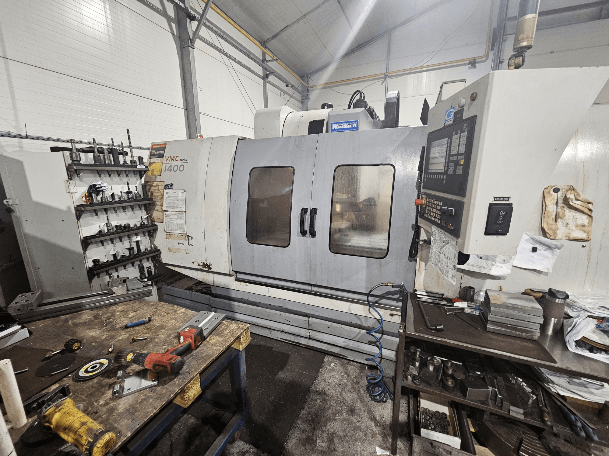 Bir atölyede VMC 1400 CNC freze makinesi, önden görünüm; yakındaki tezgah üzerine dağılmış alet ve malzemeler.