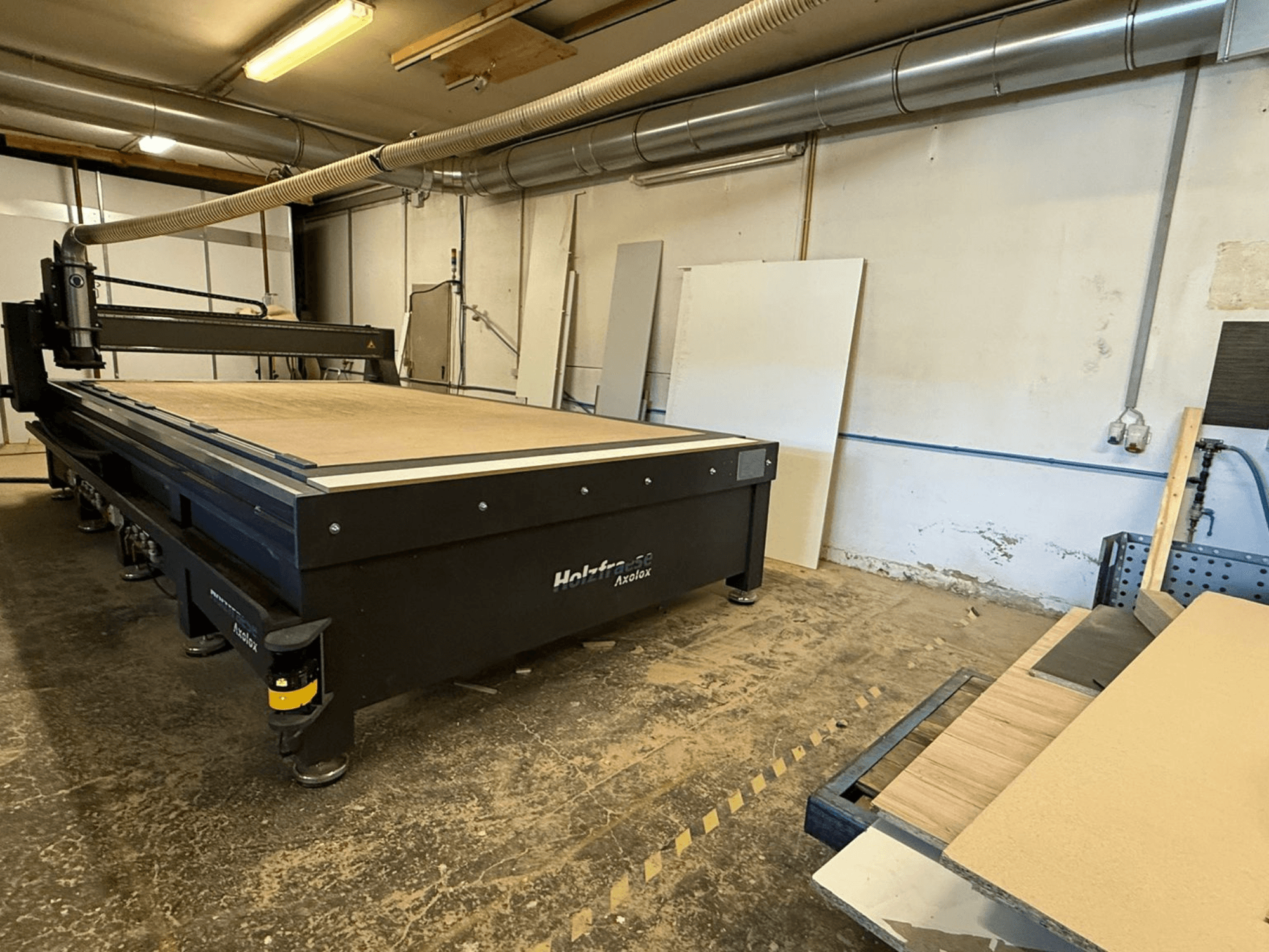Holz-Her Axos 5 CNC router atölyede, çalışma masasını, toz emme sistemini ve yakındaki ahşap panelleri gösteren önden görünüm.