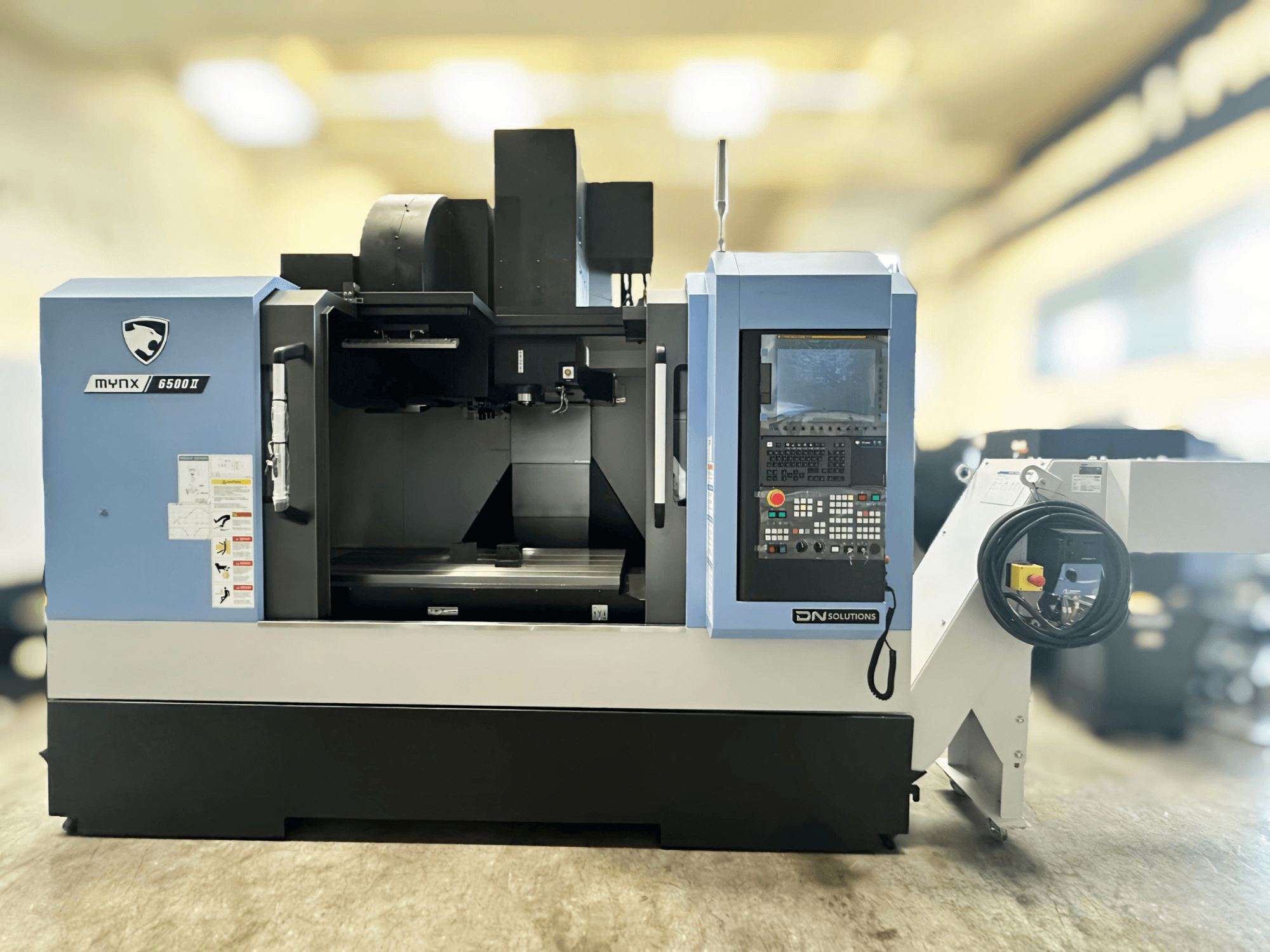 DN SOLUTIONS MYNX 6500 II dikey işleme merkezinin önden görünümü; kontrol paneli ve kullanım arayüzü ile birlikte.