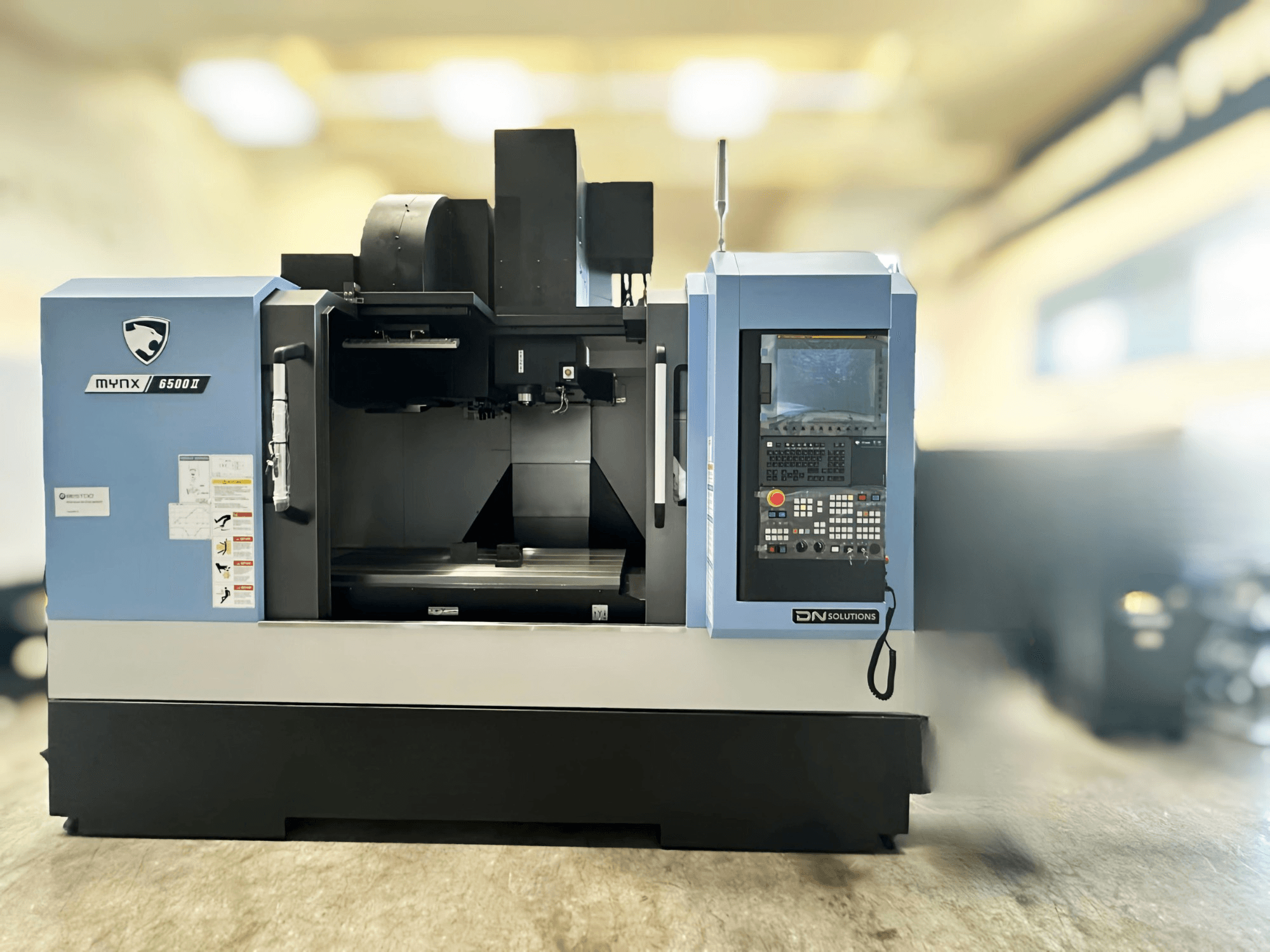 DN SOLUTIONS MYNX 6500 II dikey işleme merkezi, kontrol paneli ve çalışma alanını gösteren önden görünüm.