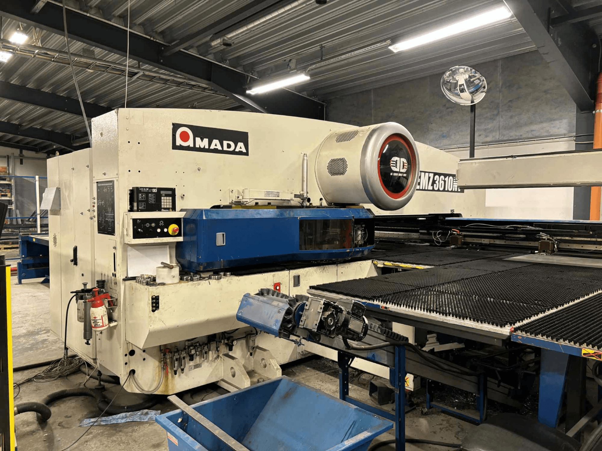 Amada EMZ3610H zımba presi önden görünüm; operasyonel kontroller, mavi yatak ve güvenlik ekipmanı özellikleri.