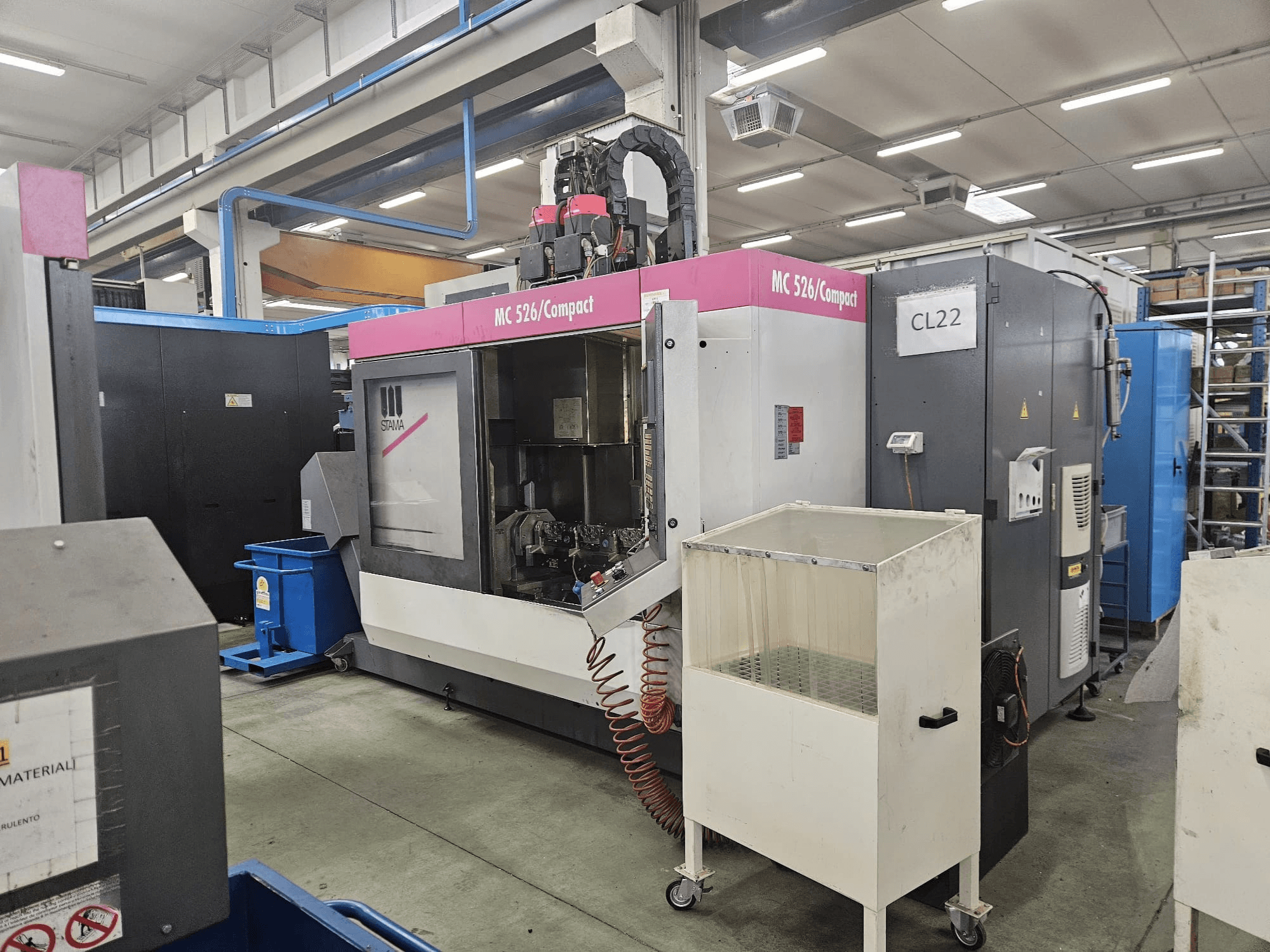 Stama'dan MC 526 Kompakt CNC makinesi, yandan görünüm, kontrol paneli, soğutucu tankı ve bitişik makineleri gösteriyor.