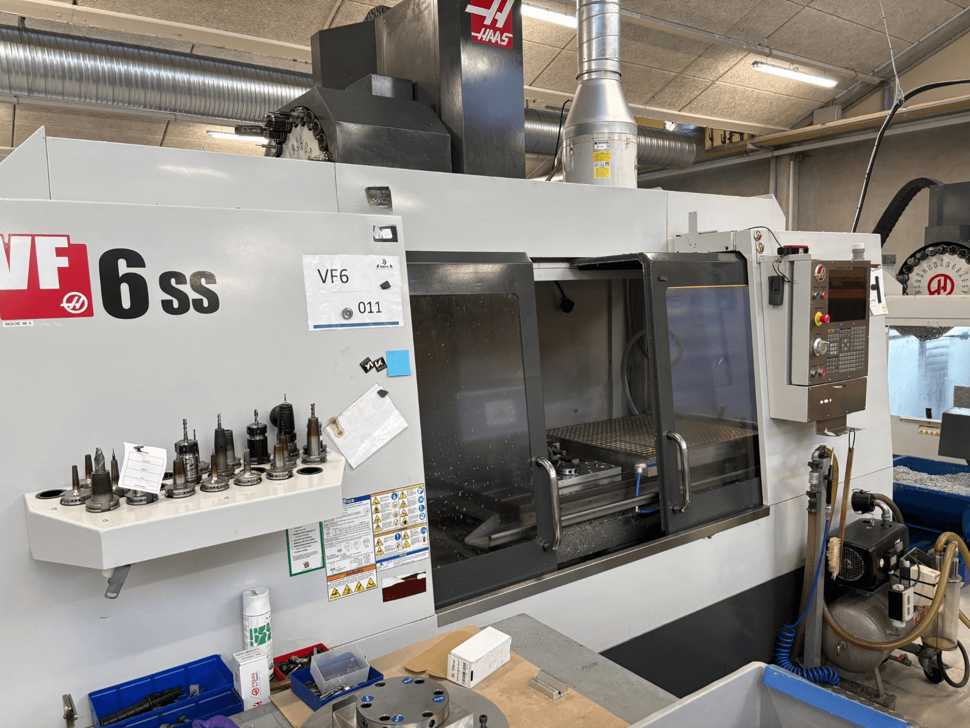 Haas VF-6 SS CNC freze makinesi, önden görünüm. Çeşitli aletler, kontrol paneli ve görünür dahili çalışma alanı.