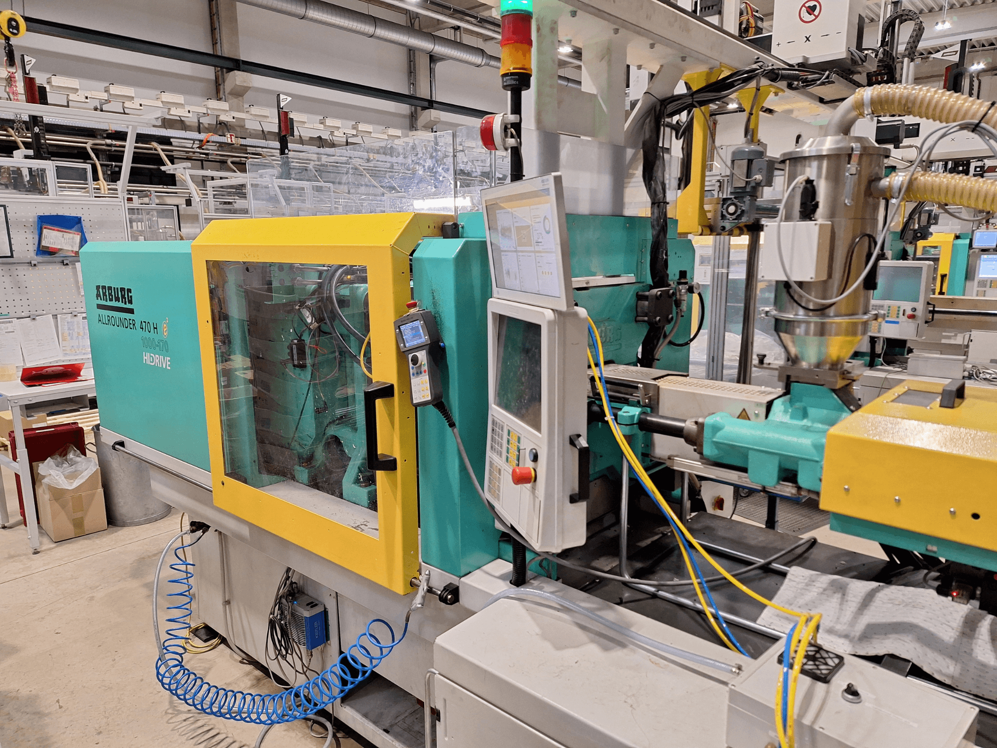 Arburg 470 H 1000-170 hidrolik enjeksiyon kalıplama makinesi, kontrol paneli ve besleme sistemini gösteren yandan görünüm.