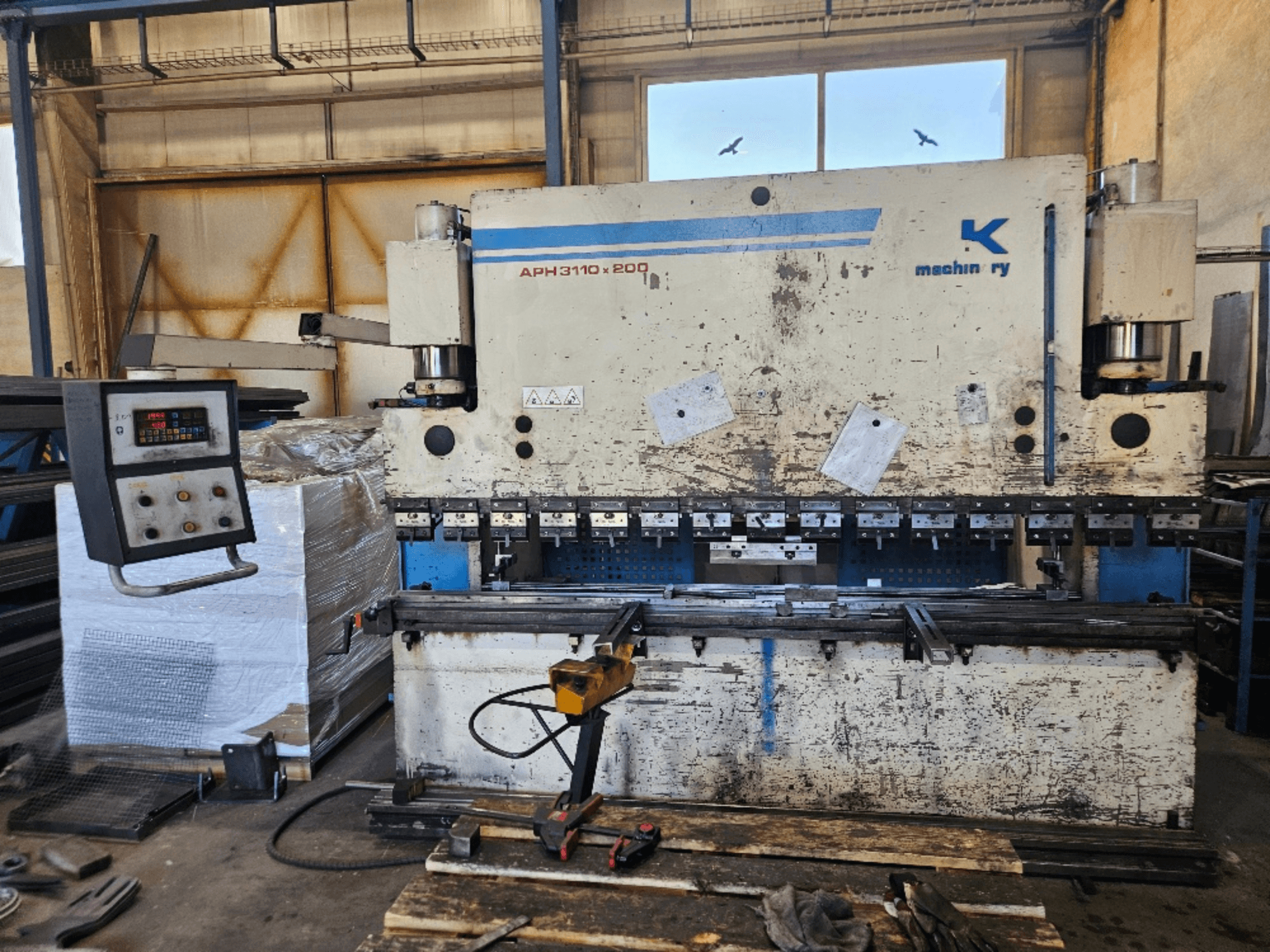 Baykal APH 3110x200 abkant pres atölyede, önden görünüm, kontrol paneli, metal levhalar ve aletler görülebilir.