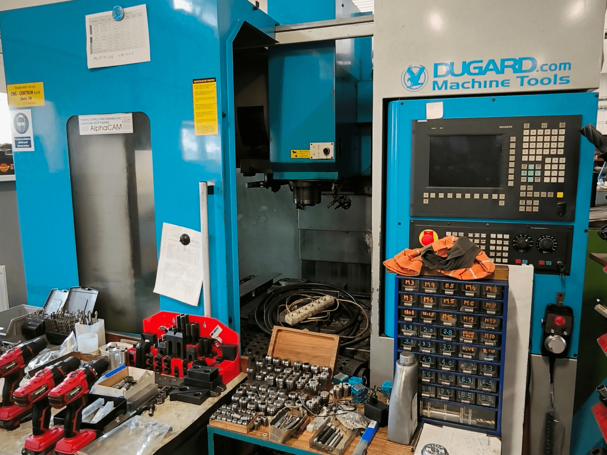 Dugard 850VMC dikey işleme merkezinin önden görünümü, kontrol paneli, takımlar ve aksesuarlar bir tezgah üzerinde gösterilmektedir.