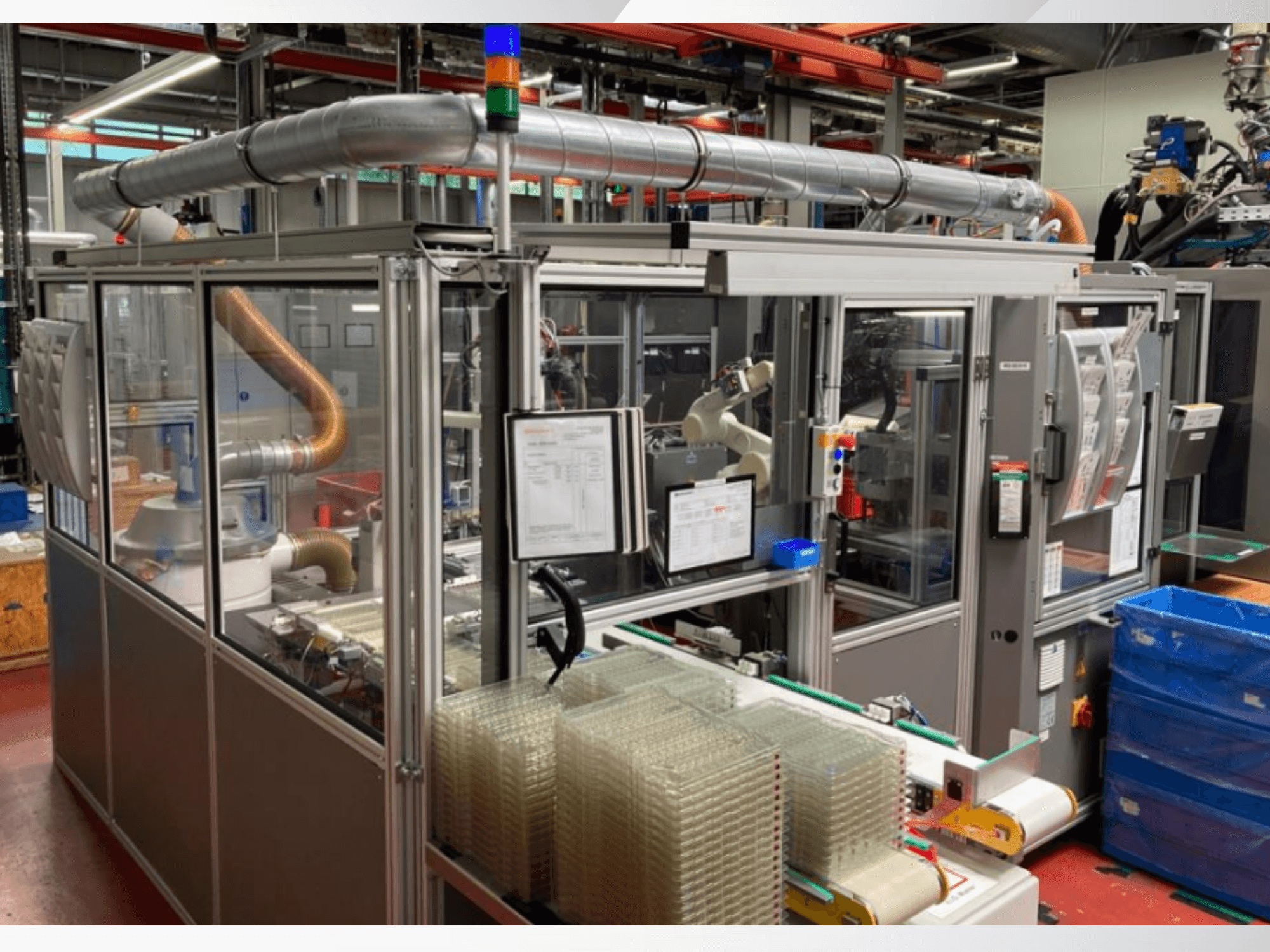 Robotik kollu otomatik montaj makinesi, şeffaf yan paneller ve şeffaf ürünlerden oluşan istiflenmiş konteynerler, önden görünüm.