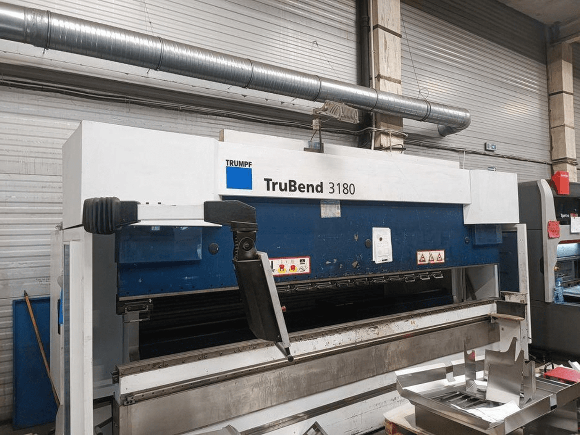 Atölyedeki Trumpf TruBend 3180 bükme makinesi, kontrol panelini ve tabla üzerindeki metal parçaları gösteren yandan görünüm.