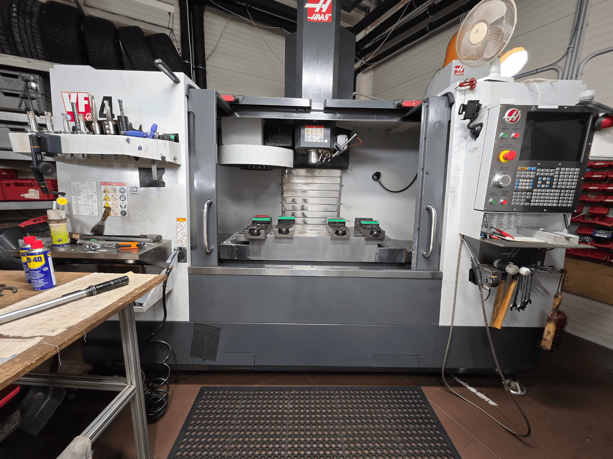 Haas VF-4 CNC frezenin atölyedeki önden görünümü; aletler, bilgisayar arayüzü ve tabla üzerinde iki iş parçası.