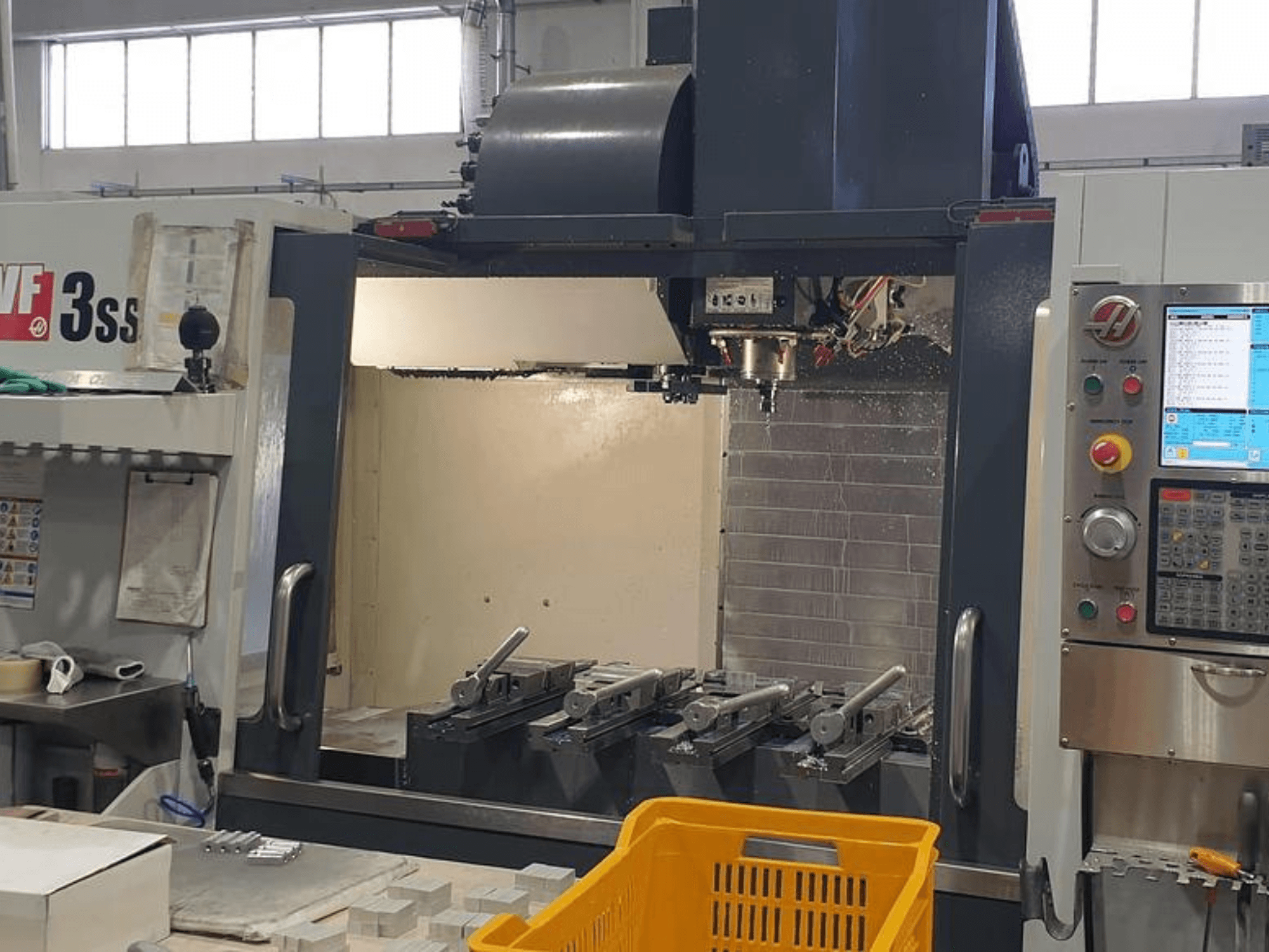 HAAS VF-3SS dikey işleme merkezi, CNC kontrol paneli, takımlar ve turuncu sepet ile önden görünüm.