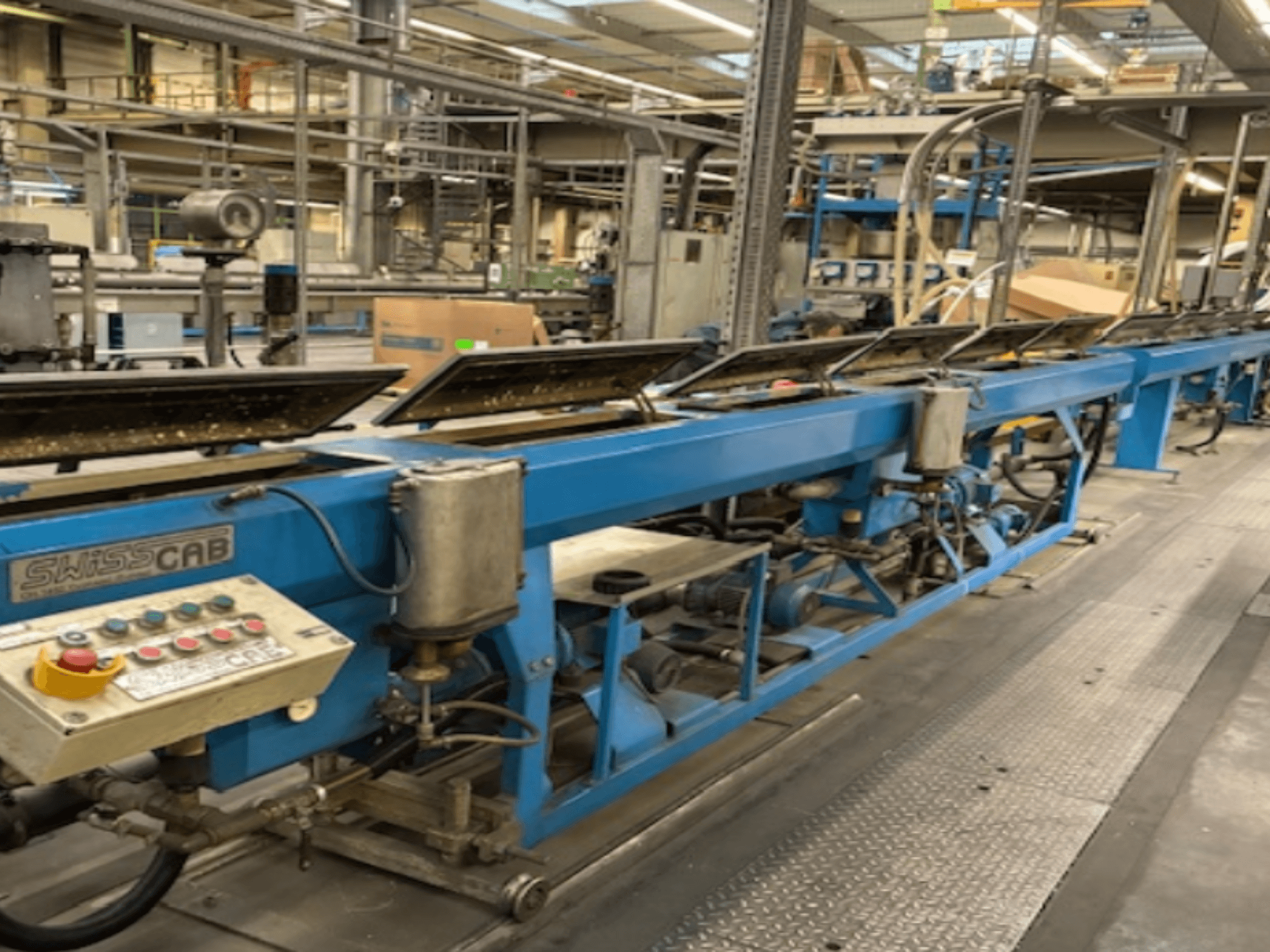 Fabrika ortamında mavi SwissCab endüstriyel makine, çalışma düğmeleri ve konveyör sistemi, yandan görünüm.