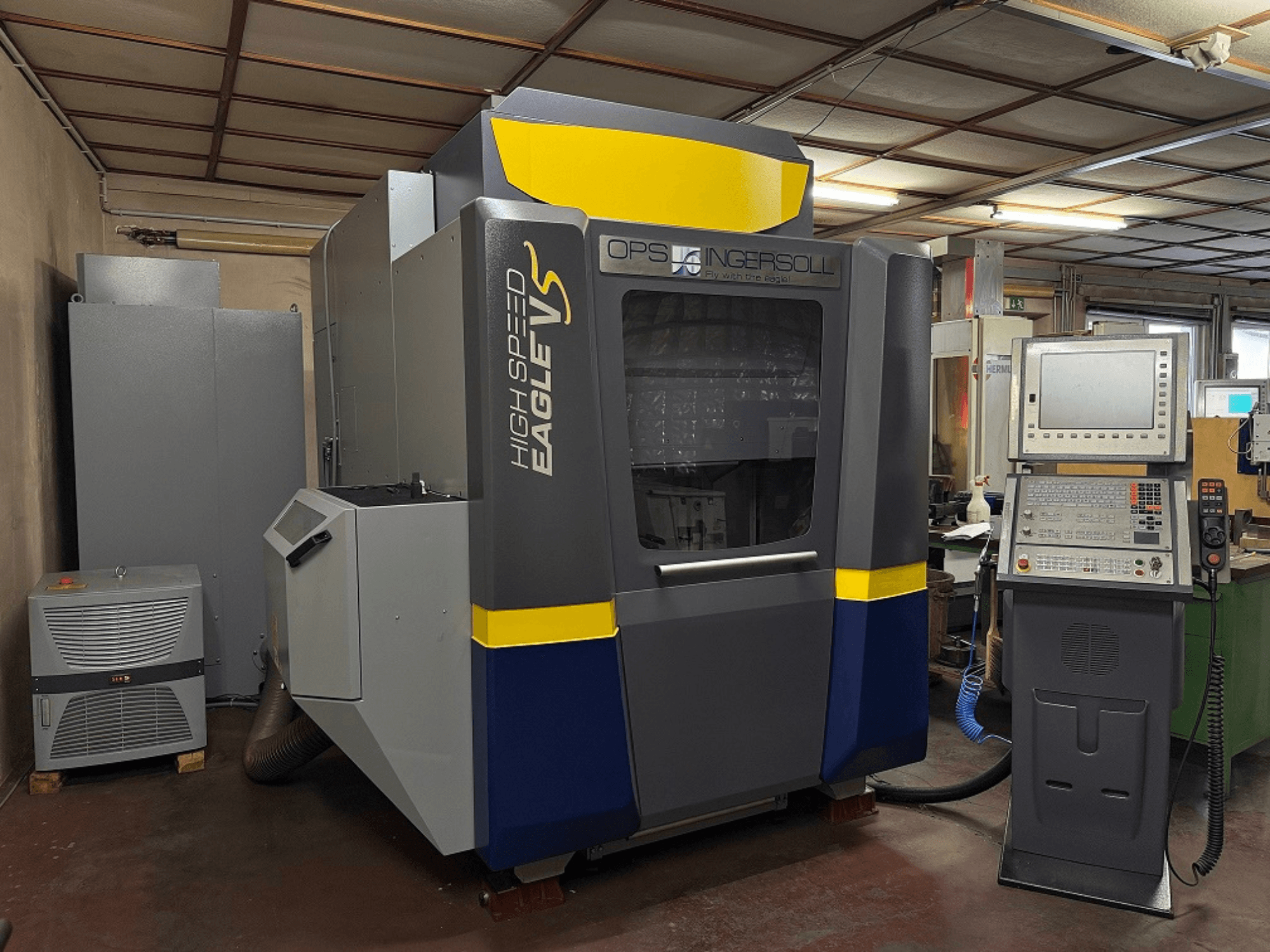 OPS Ingersoll'un Yüksek Hızlı Eagle V makinesi, yandan görünüm, kontrol paneli ve endüstriyel ortamda bitişik ekipman.