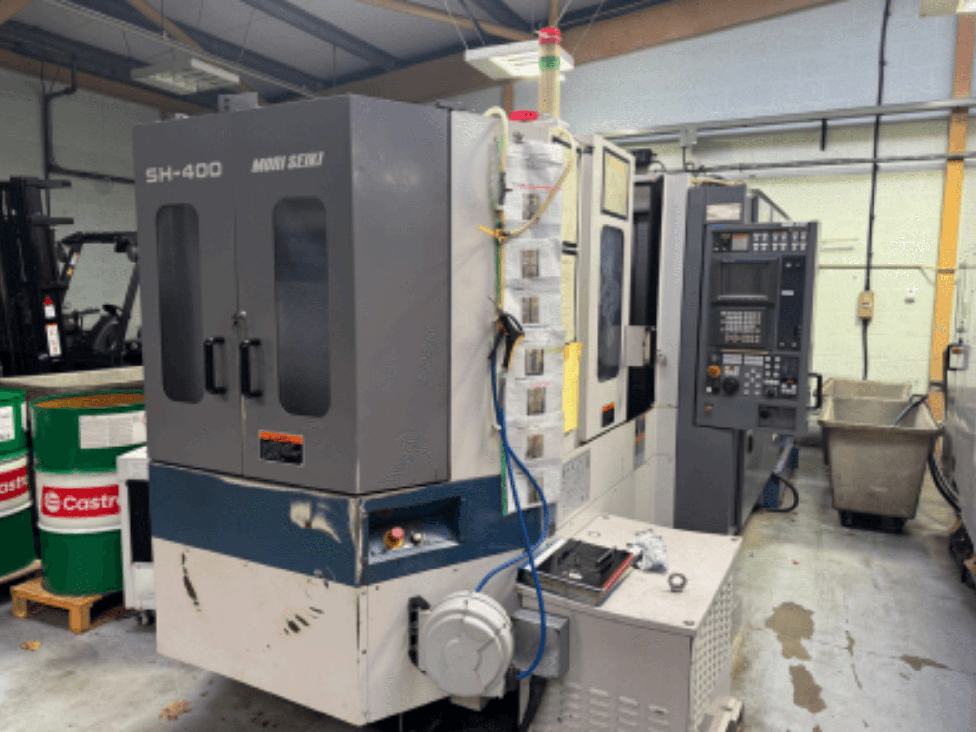 Moni Seiki SH-400 CNC makinesi, kontrol panelini, kapıları ve çevresindeki endüstriyel ortamı gösteren yandan görünüm.