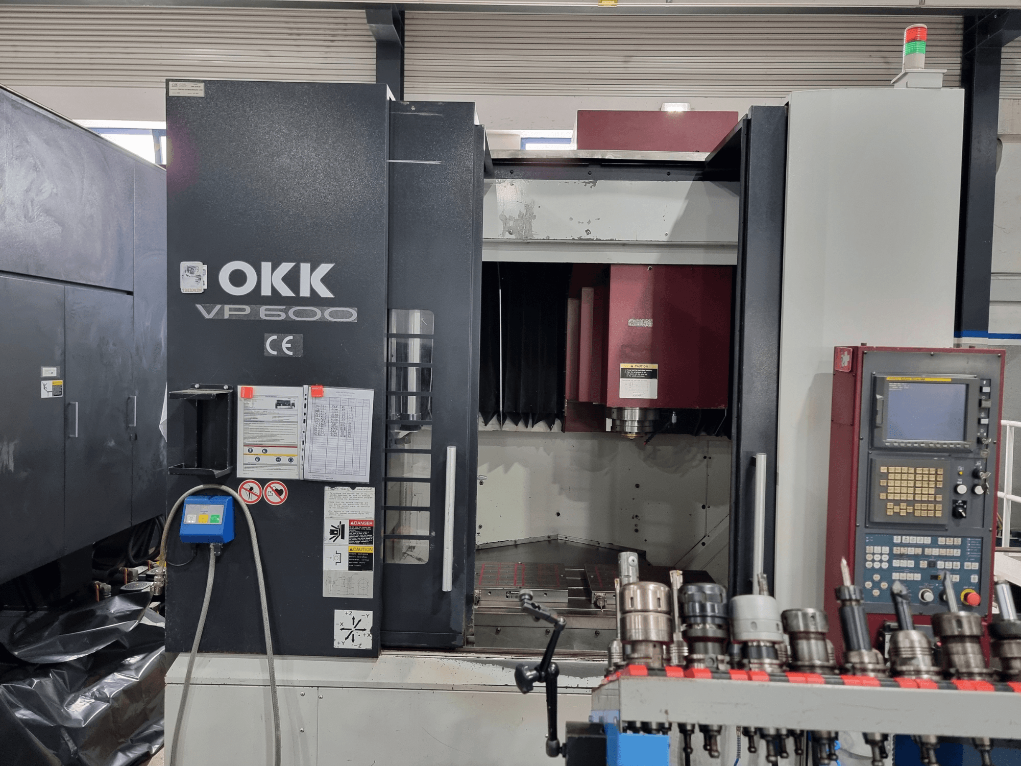 OKK VP600 dikey işleme merkezinin önden görünümü; kontrol paneli ve rafa monte edilmiş takım tutucular gösterilmektedir.