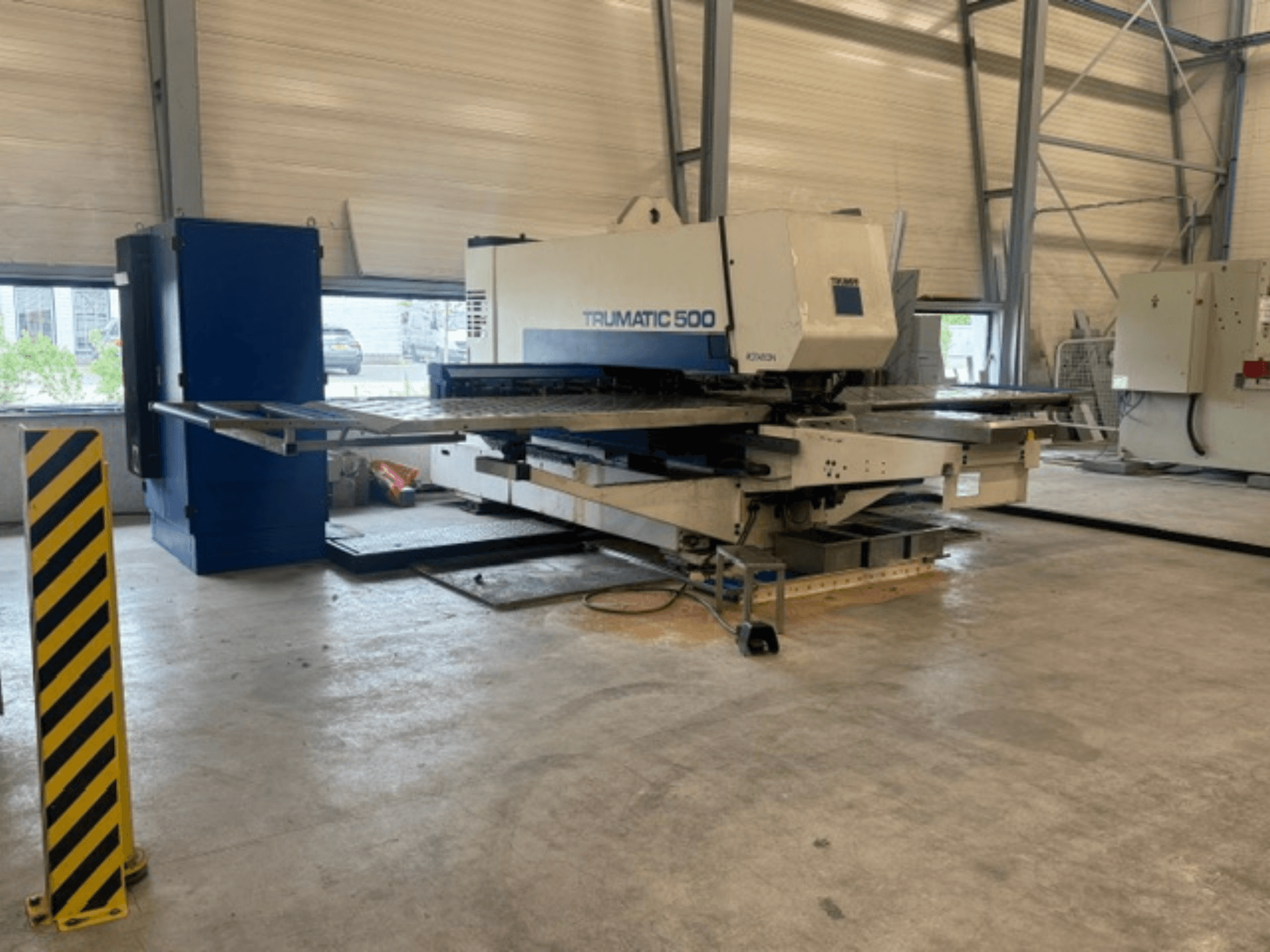 Bir atölyede bulunan TRUMPF Trumatic 500 CNC delme makinesi; makineyi ve sarı şeritli güvenlik direğini gösteren yandan görünüm.