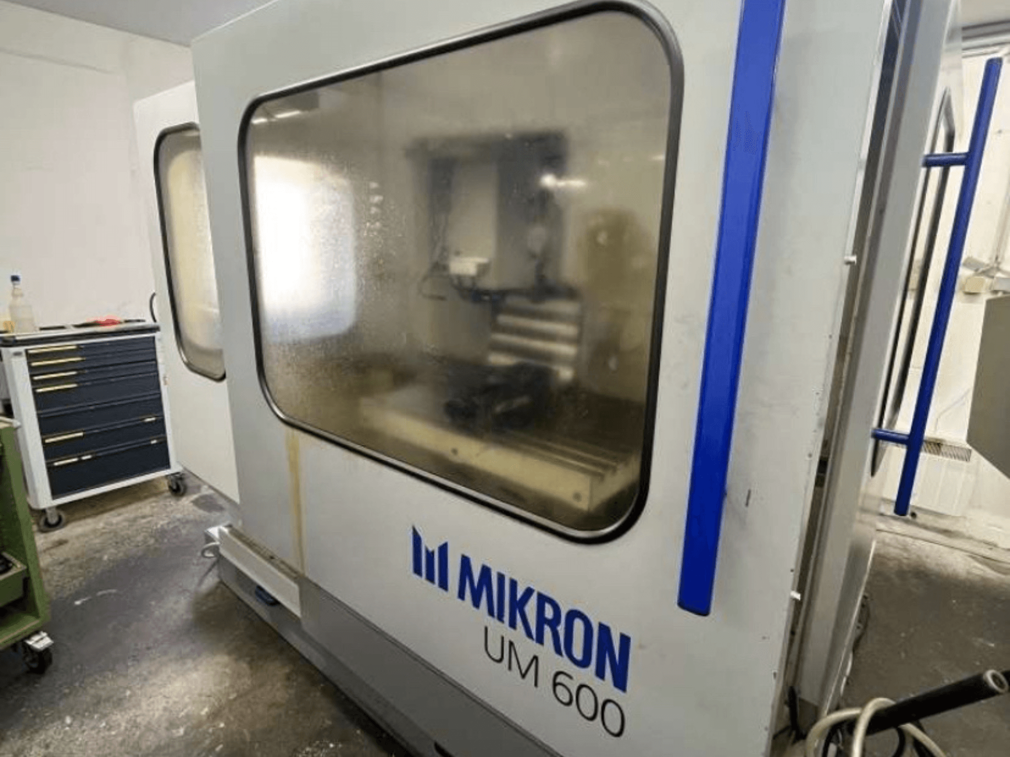 MIKRON UM 600 TNC 410/426 üniversal işleme merkezi, yandan görünüm, buğulu cam ve yanında görünür takım saklama yeri.