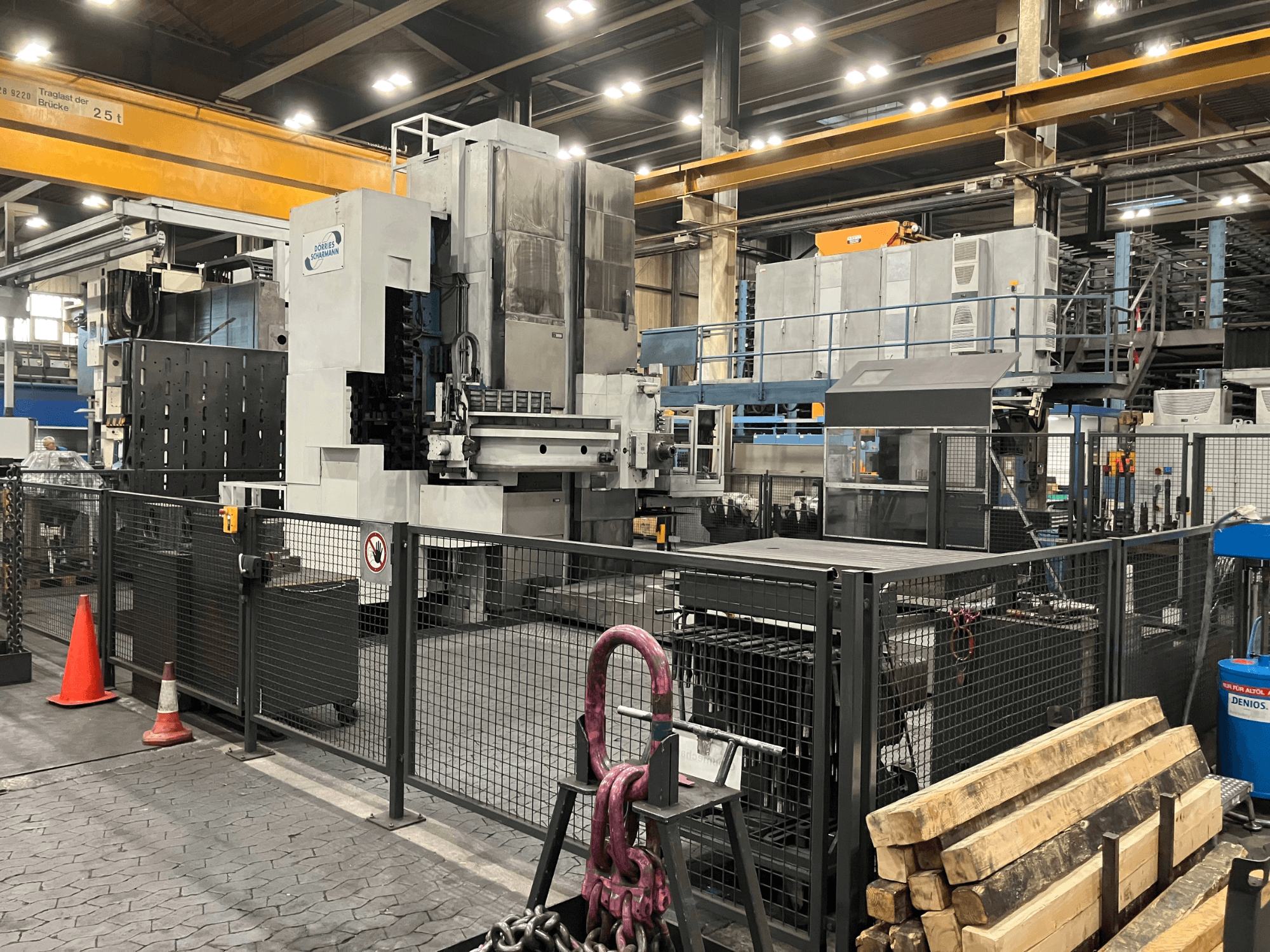 Fabrika ortamında bulunan DÖRRIES SCHARMANN Heavycut 1.2 TDV4 delme makinesi; güvenlik bariyerleri ve yakınında bulunan aletlerle birlikte yandan görünüm.