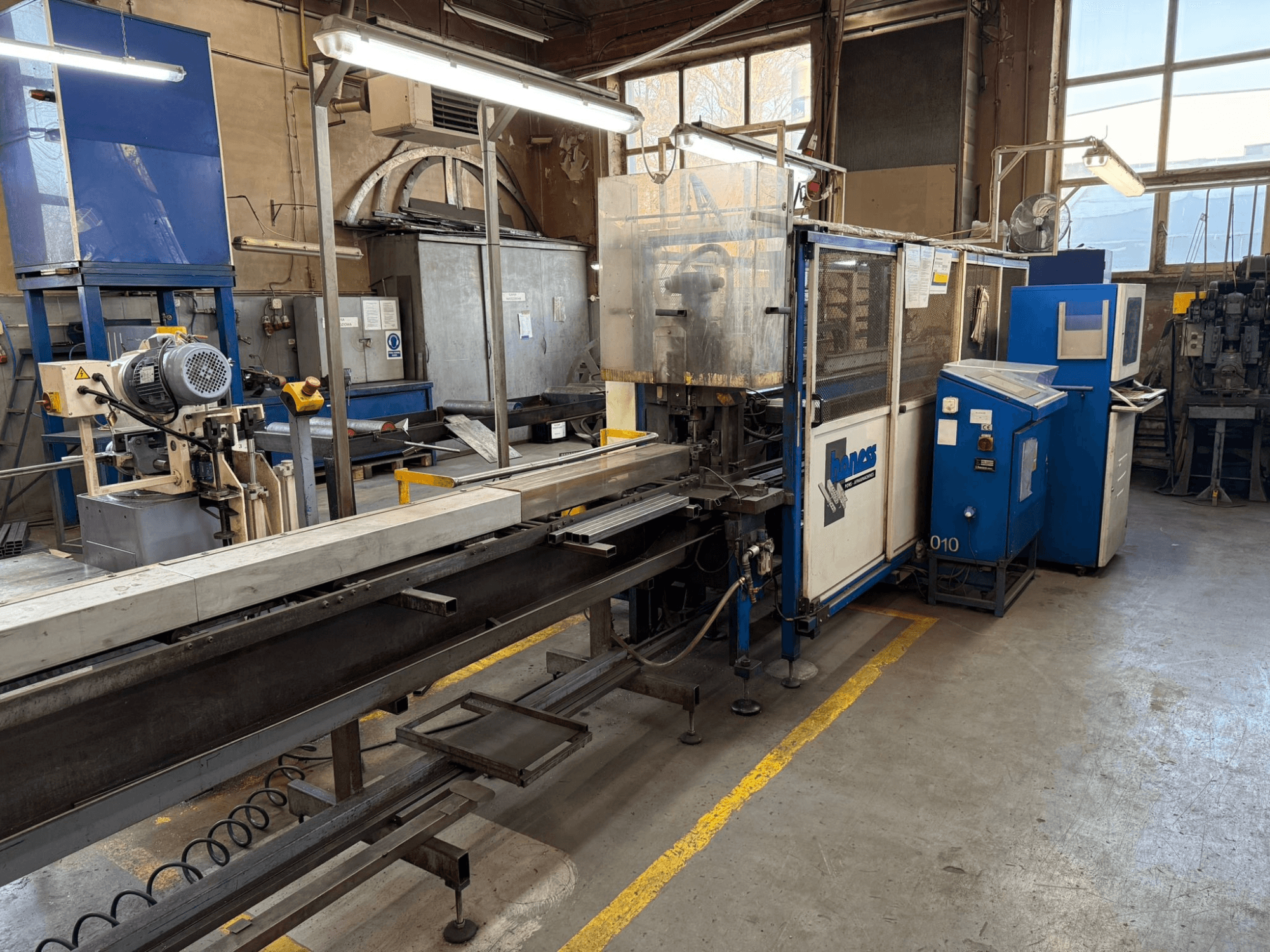 Mavi bir Haweas makinesine sahip endüstriyel atölye, geniş ve iyi aydınlatılmış bir alanda konveyör ve ekipmanı gösteren yandan görünüm.