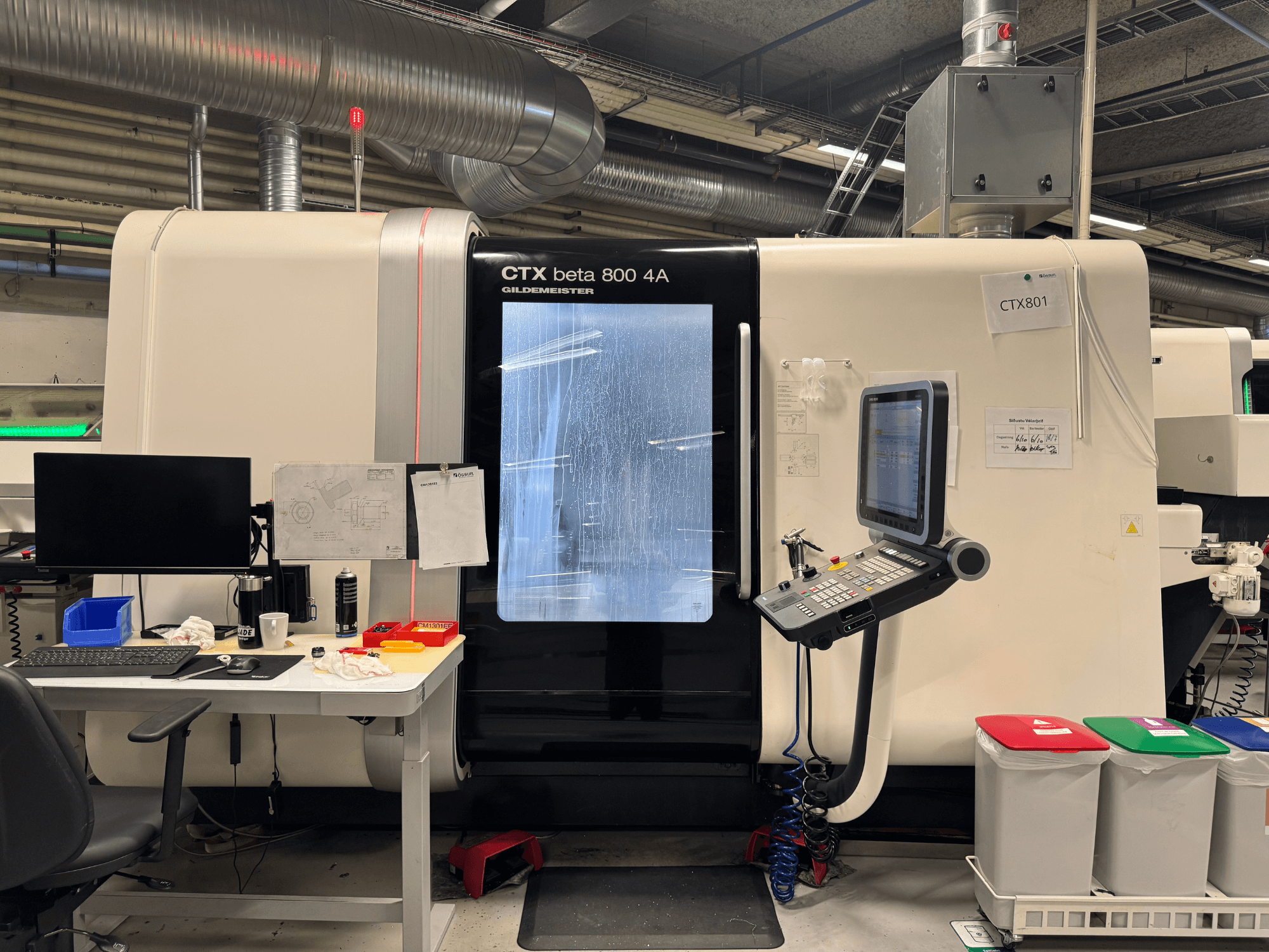 CTX beta 800 4A makine, kontrol paneli ve monitörle birlikte, yandan görünüm, ofis düzeneği ve renkli çöp kutuları olan bir atölyede.