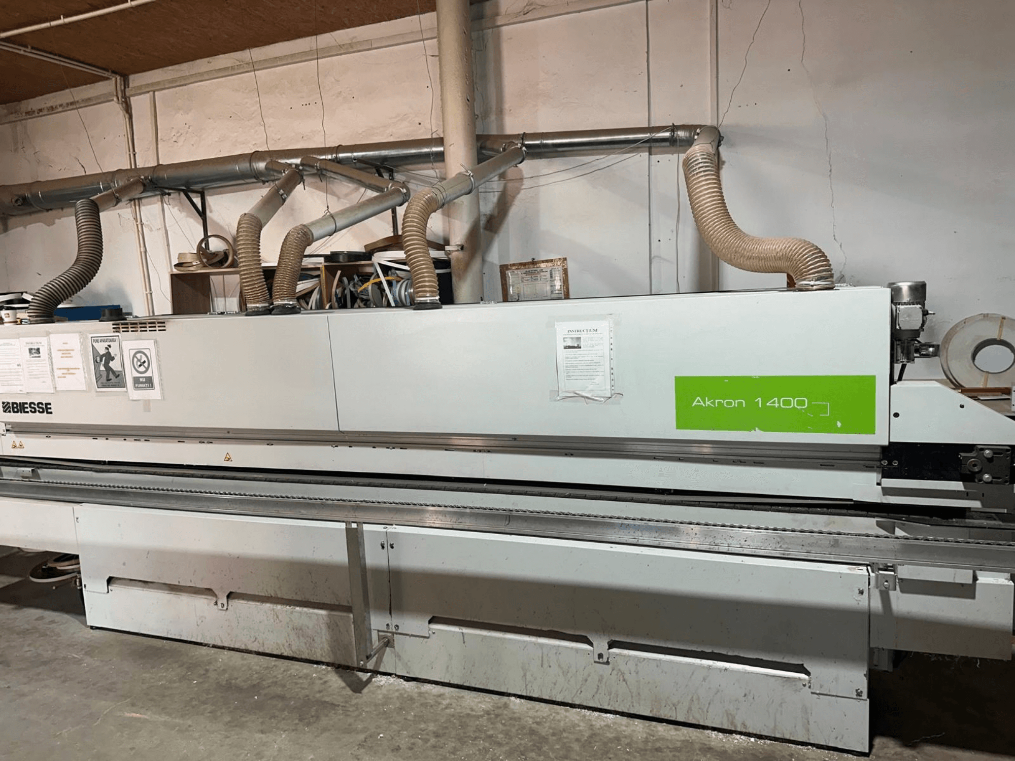 BIESSE Akron 1440 A kenar kaplama makinesinin yandan görünümü; havalandırma kanalları, kontrol paneli ve kullanım etiketleri ile birlikte.