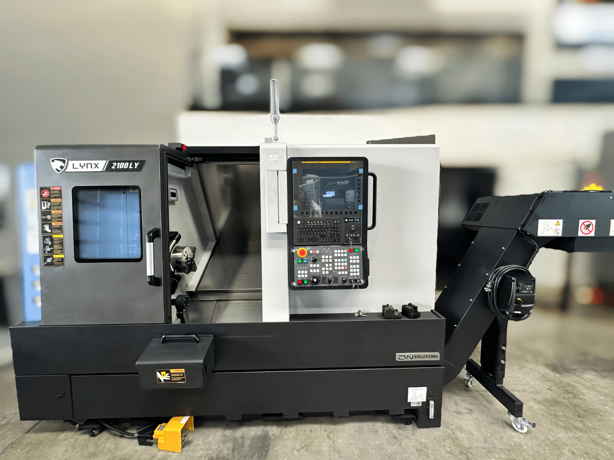 Yatay tornalama makinesi DN SOLUTIONS LYNX 2100LYB, önden görünüm, kontrol paneli ve iç kısmı gösteren açık kapı.