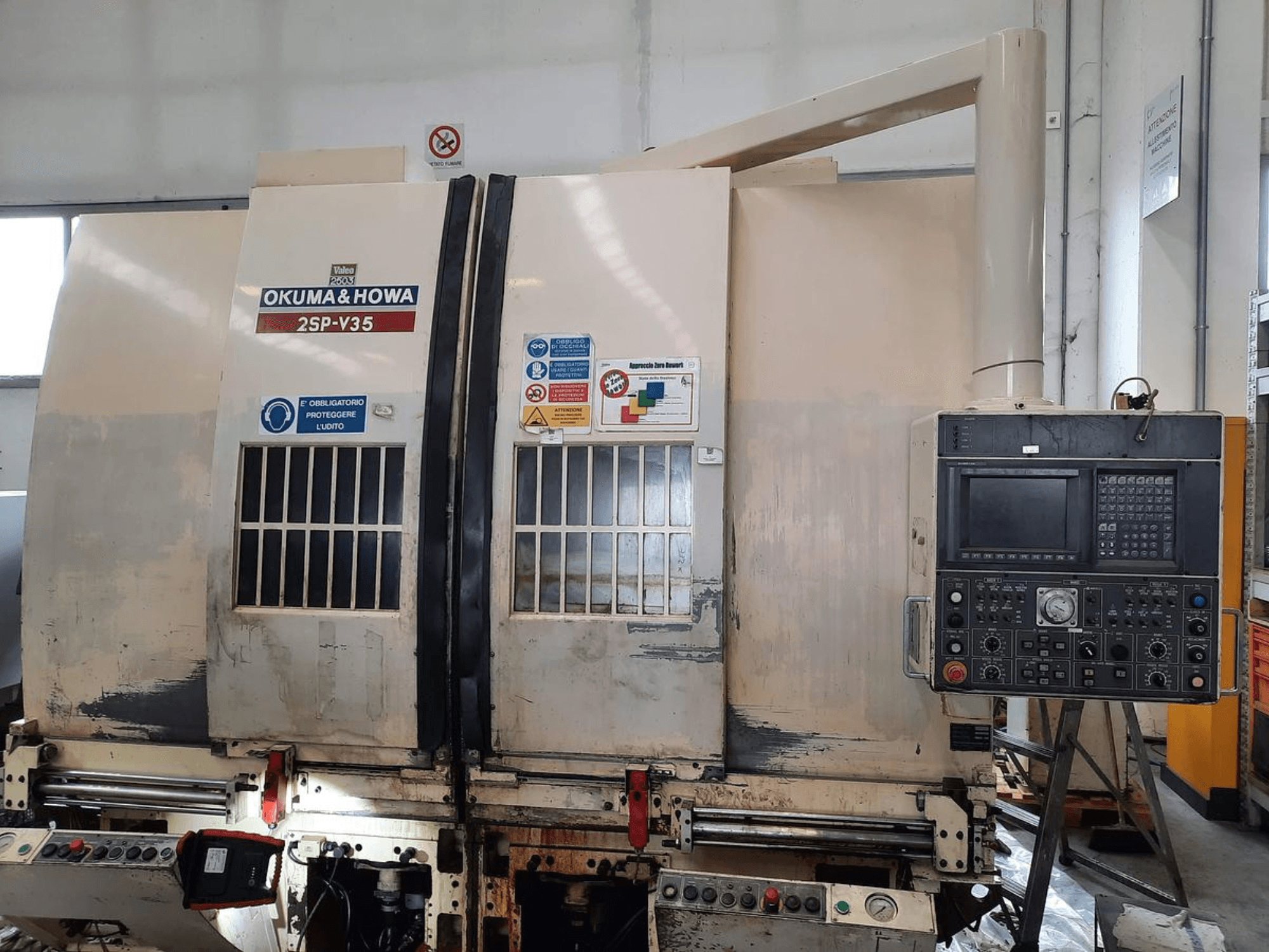 OKUMA & HOWA 2SP-V35 CNC makinesi önden bakıldığında, çeşitli düğmeler ve güvenlik etiketleri içeren kontrol paneline sahiptir.