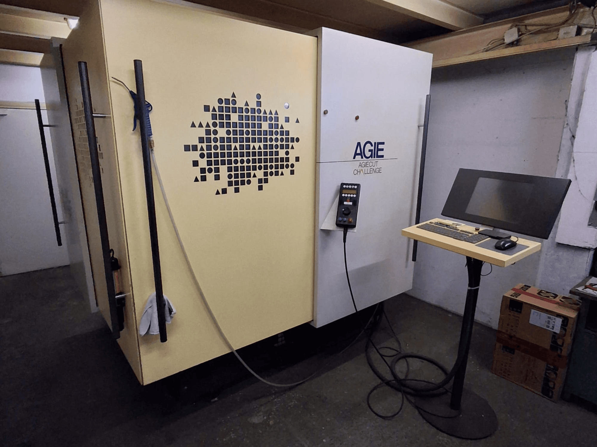 Bir atölyede bulunan AGIE Agiecut Challenge 2 telli EDM makinesi; kontrol paneli ve monitörün bir stand üzerinde yer aldığı ön görünüm.