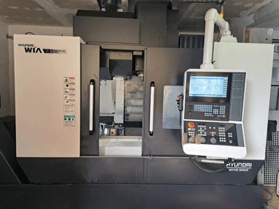 Hyundai WIA F500 Plus CNC makinesinin önden görünümü, dijital kontrol paneli ve güvenlik etiketleri.