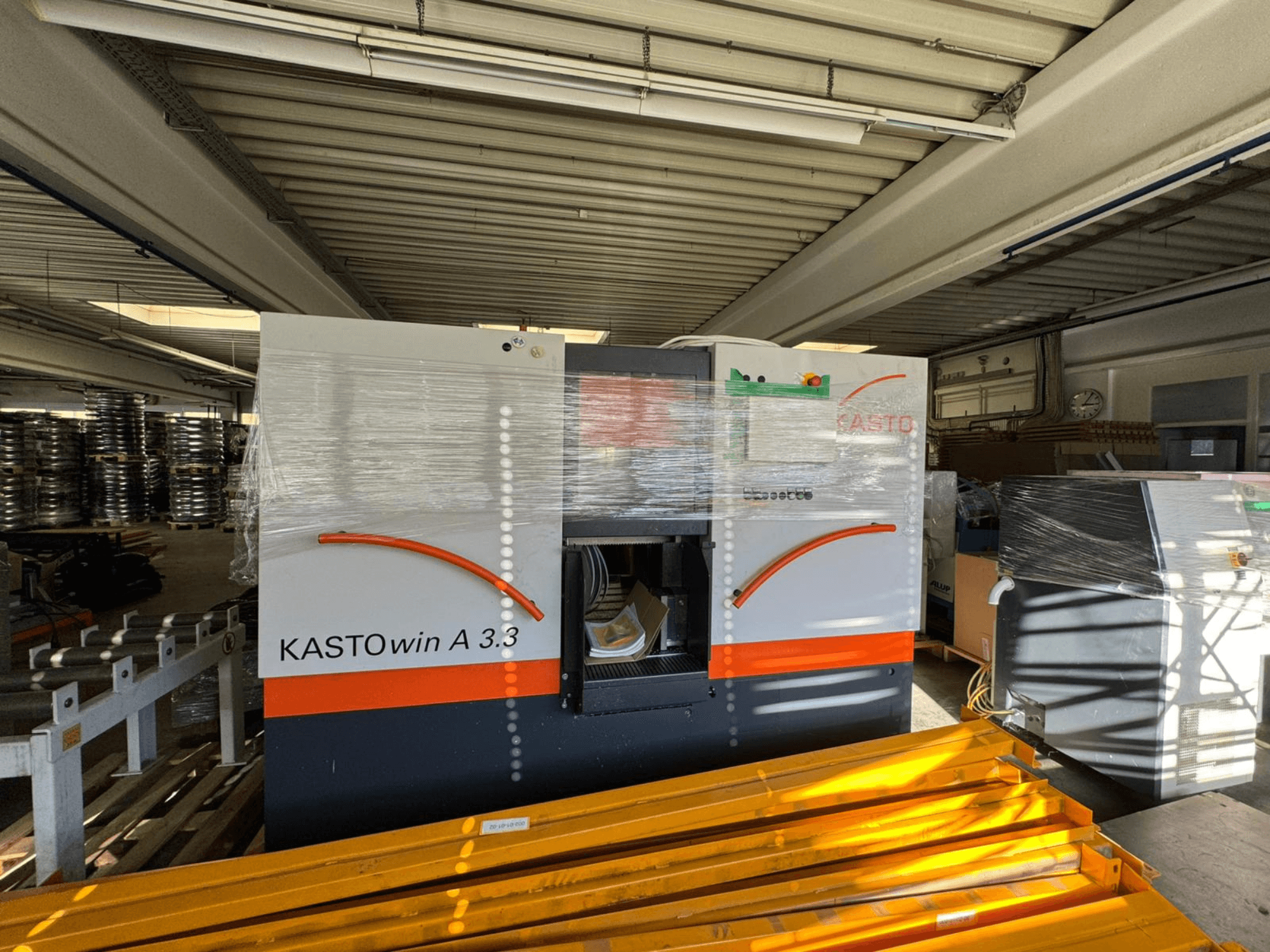 KASTO A 3.3 metal şerit testeresinin önden görünümü; koruma amacıyla ambalajlanmış halde, çalıştırma kumandaları ve çevresindeki ekipmanlar görülebilir durumda.