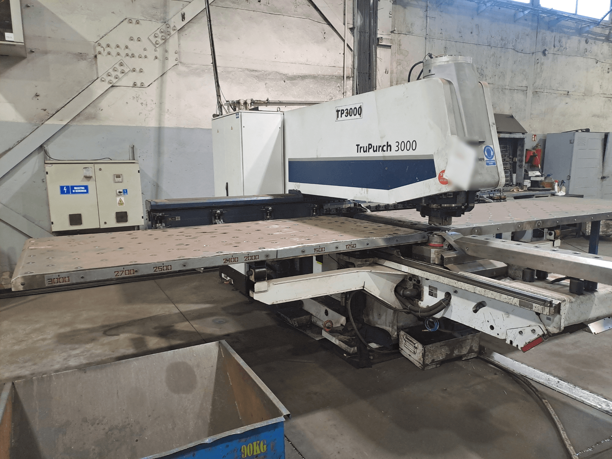 TruPunch 3000 CNC makinesi, büyük bir metal plaka ve ölçüm işaretleri ile endüstriyel bir ortamda önden gösterilmiştir.