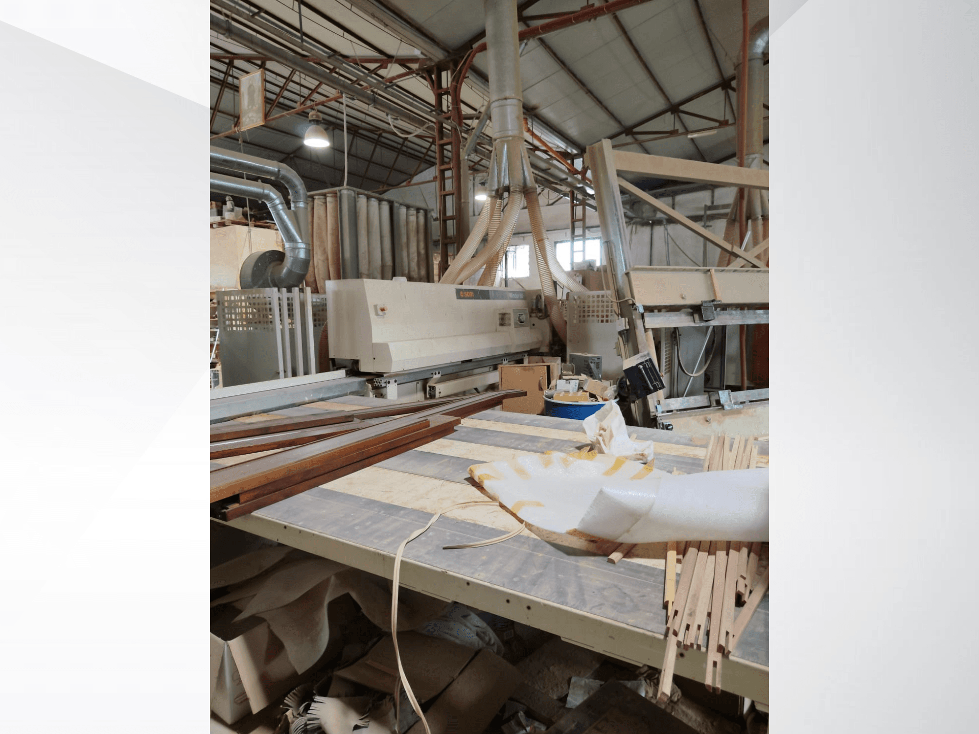 CNC Ahşap İşleme Merkezi SCM Windor60, ahşap paneller ve toz emme ekipmanı ile yandan bakıldığında bir atölyede.