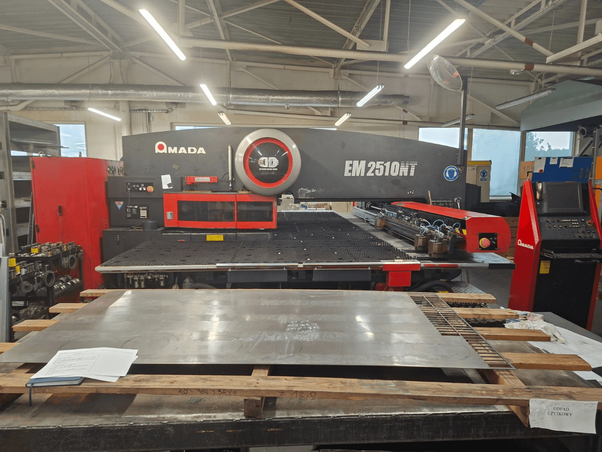 AMADA EM 2510NT taret zımba presinin önden görünümü, metal levha ve kontrol paneli bir atölye ortamında görülebilir.