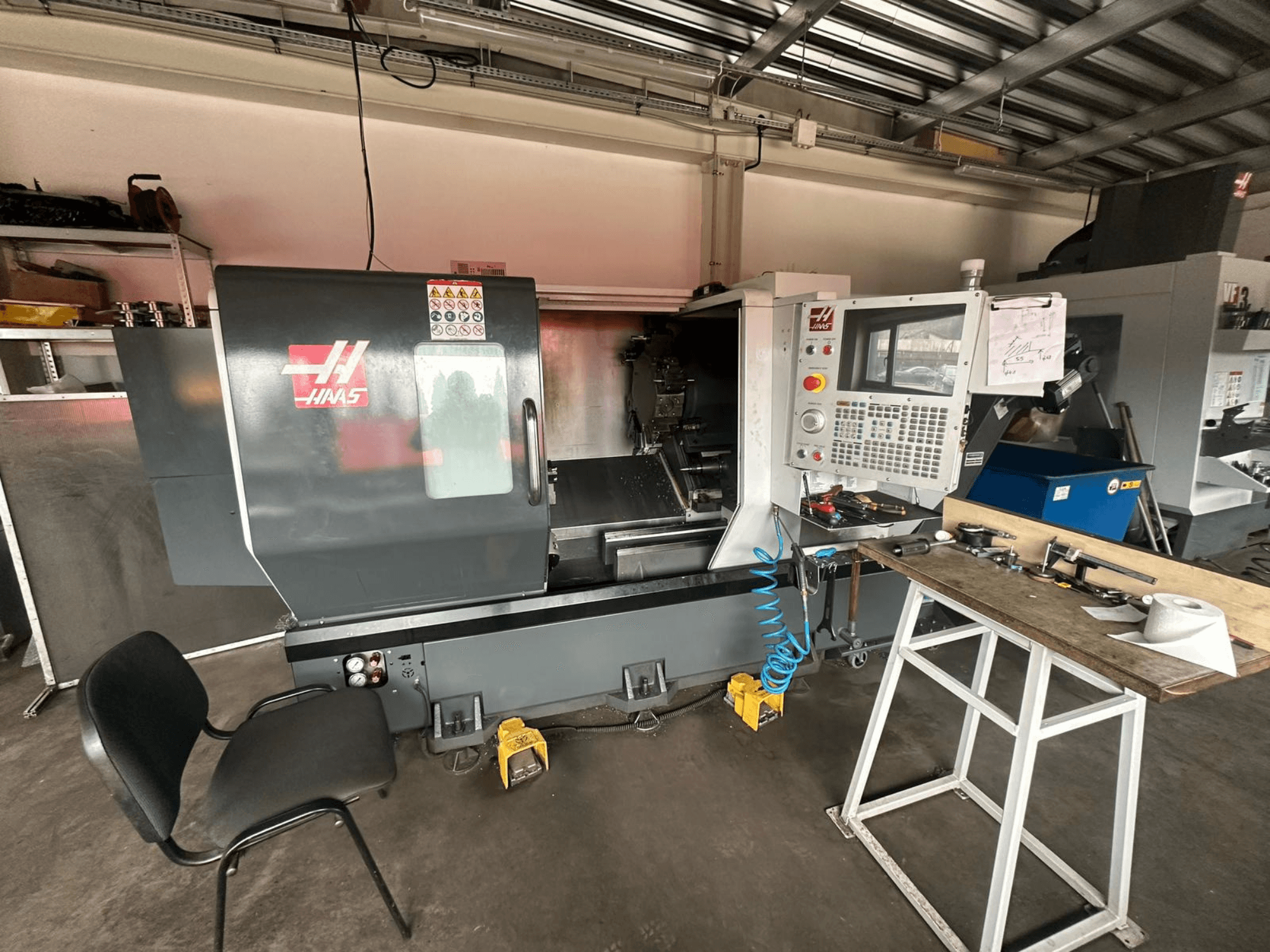 Bir atölyede Haas CNC torna tezgahı (model ST-10), kontrolleri gösteren yandan görünüm, tezgah üzerinde aletler ve yanında bir sandalye.
