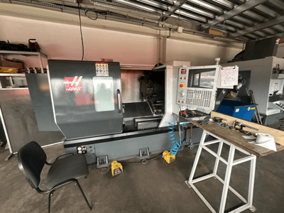 Bir atölyede Haas CNC torna tezgahı (model ST-10), kontrolleri gösteren yandan görünüm, tezgah üzerinde aletler ve yanında bir sandalye.