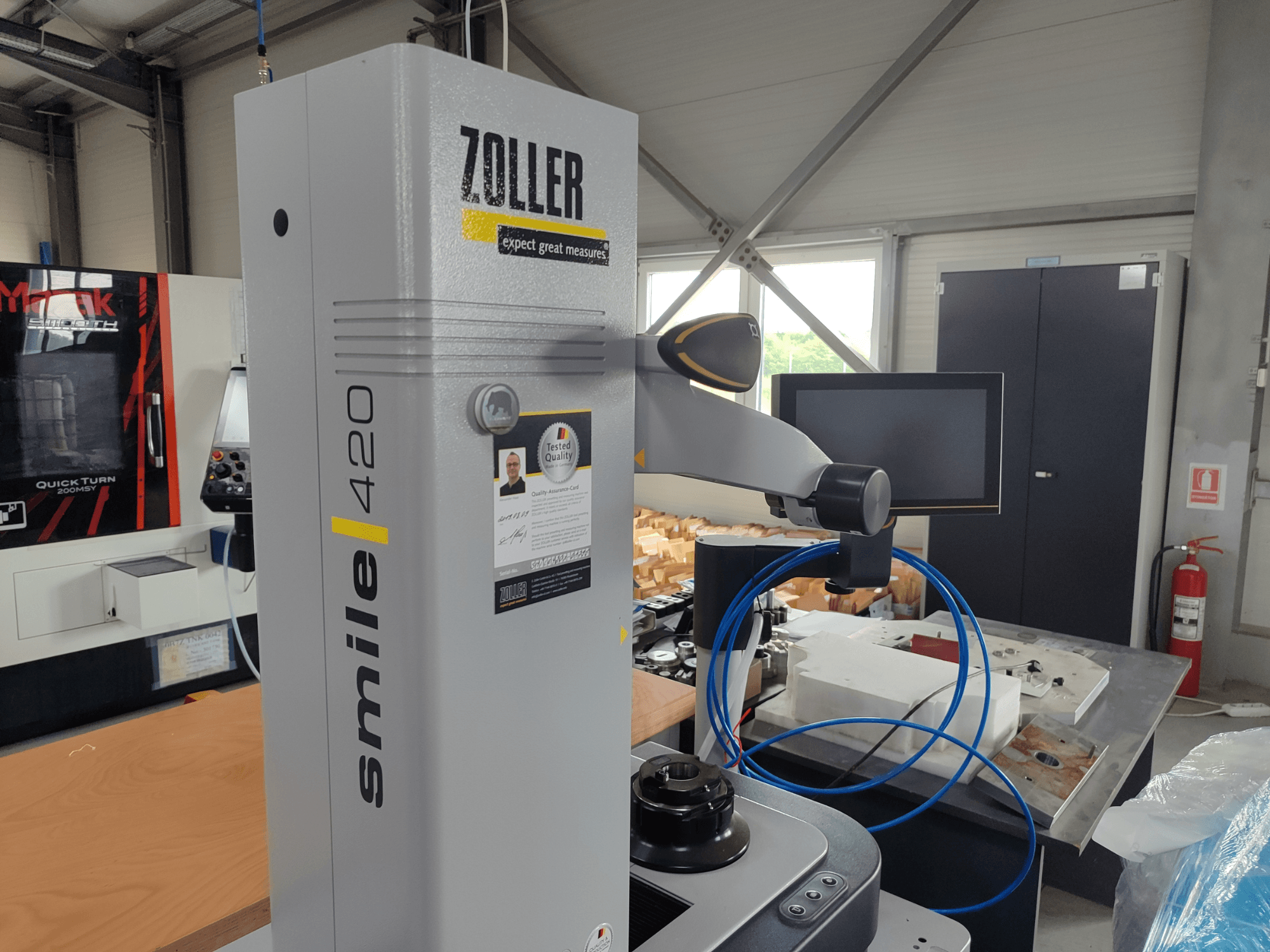ZOLLER smile 420 monitörlü ölçüm cihazı, atölyede yandan görünüm, arka planda mavi hortumlar ve makineler.