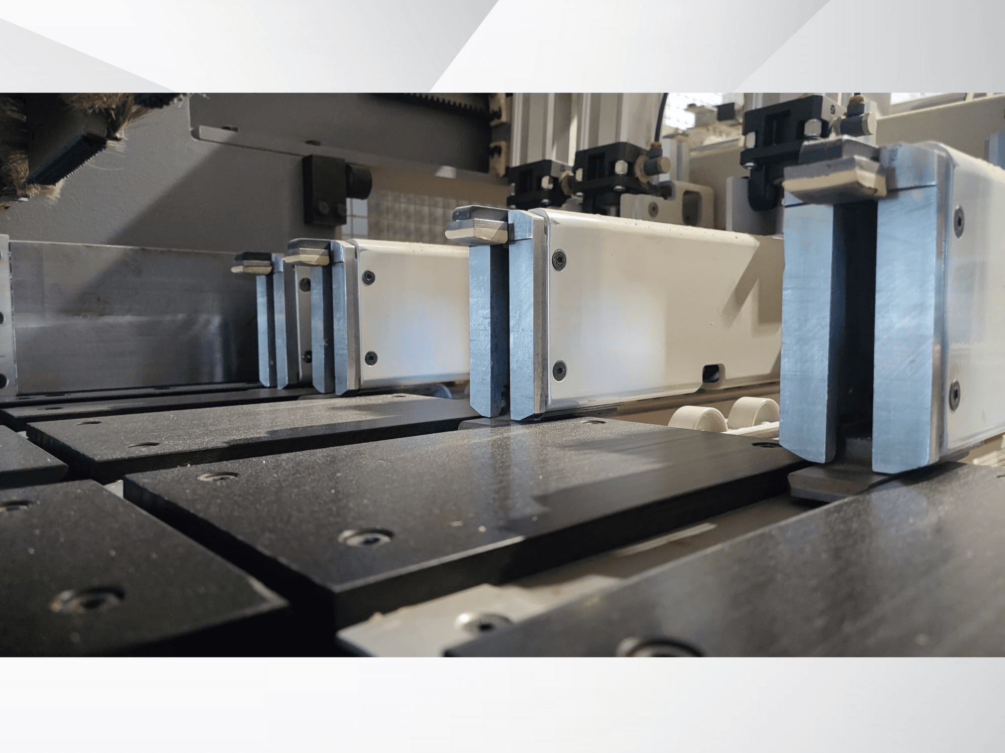 Siyah çalışma yüzeylerine ve görünür kılavuz raylara sahip, metalik çeneli hassas bir makinenin sıkıştırma mekanizmasının yakından görünümü.