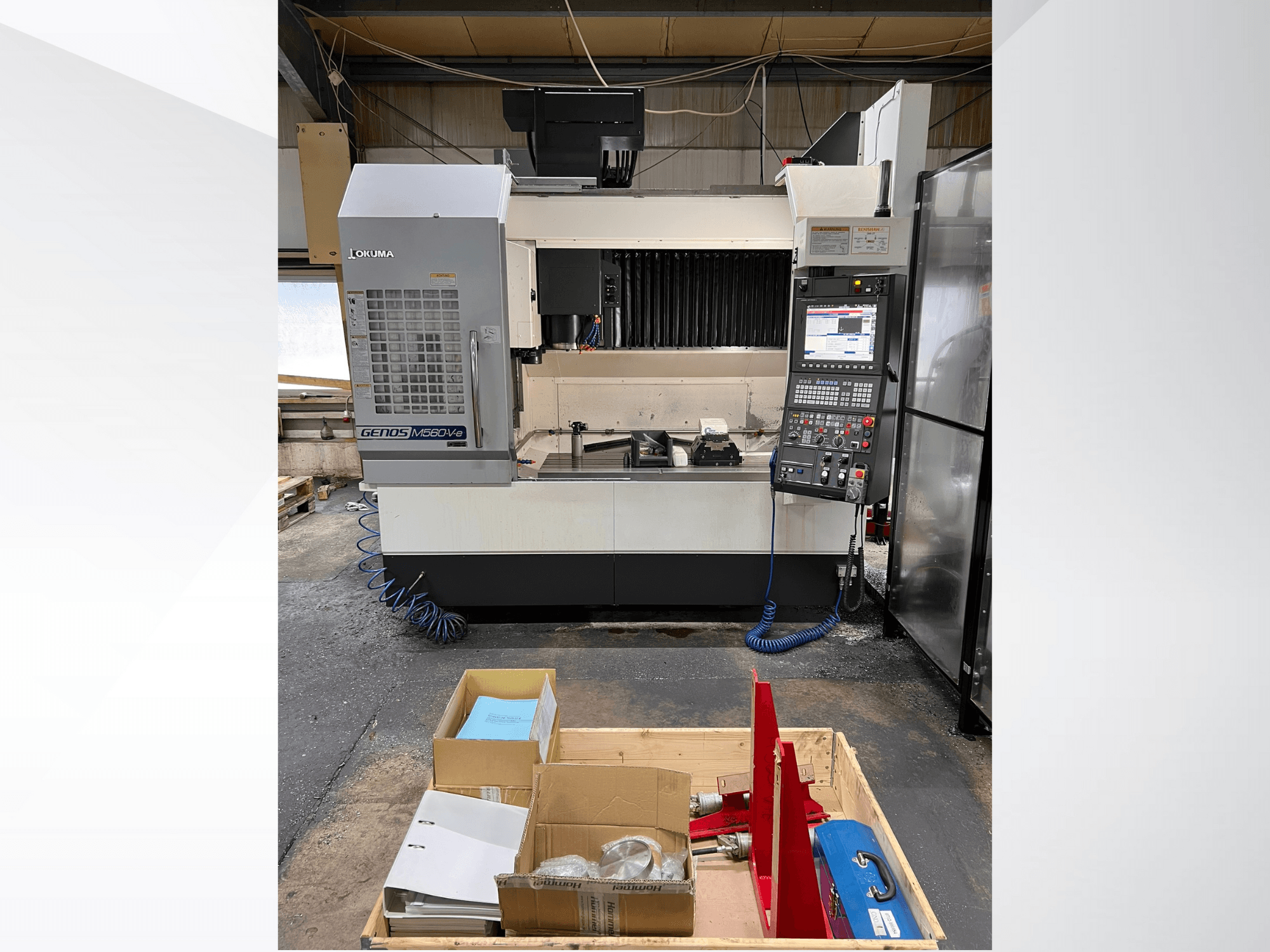 Okuma GENOS M460V-5 dikey işleme merkezi, önden görünüm, kontrol paneli görünür ve takımlar çalışma tezgahında.