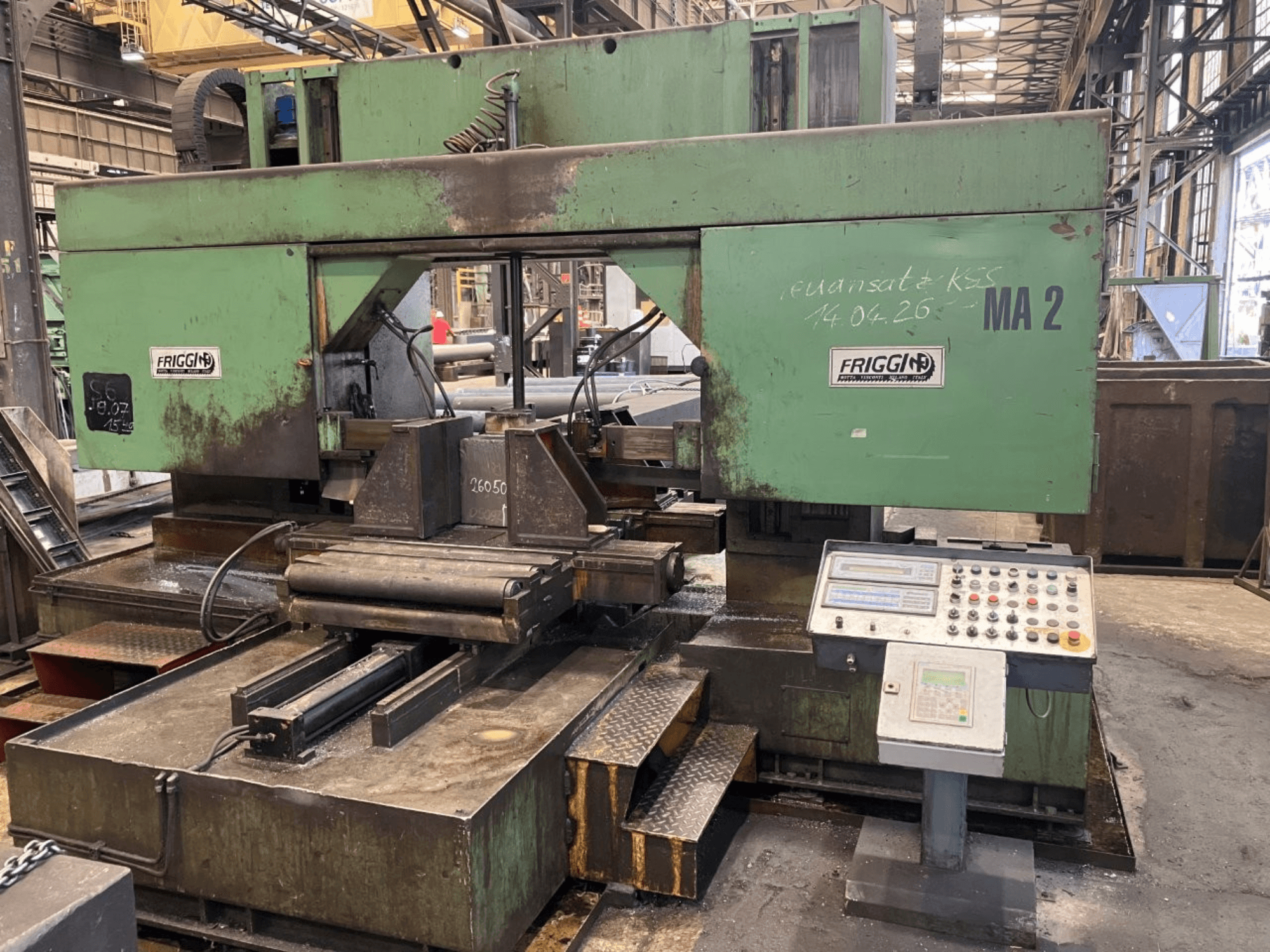 Friggi 2MF/AUT metal şerit testere; atölye ortamında kontrol paneli, testere bıçağı bölümü ve masa düzenini gösteren önden görünüm.