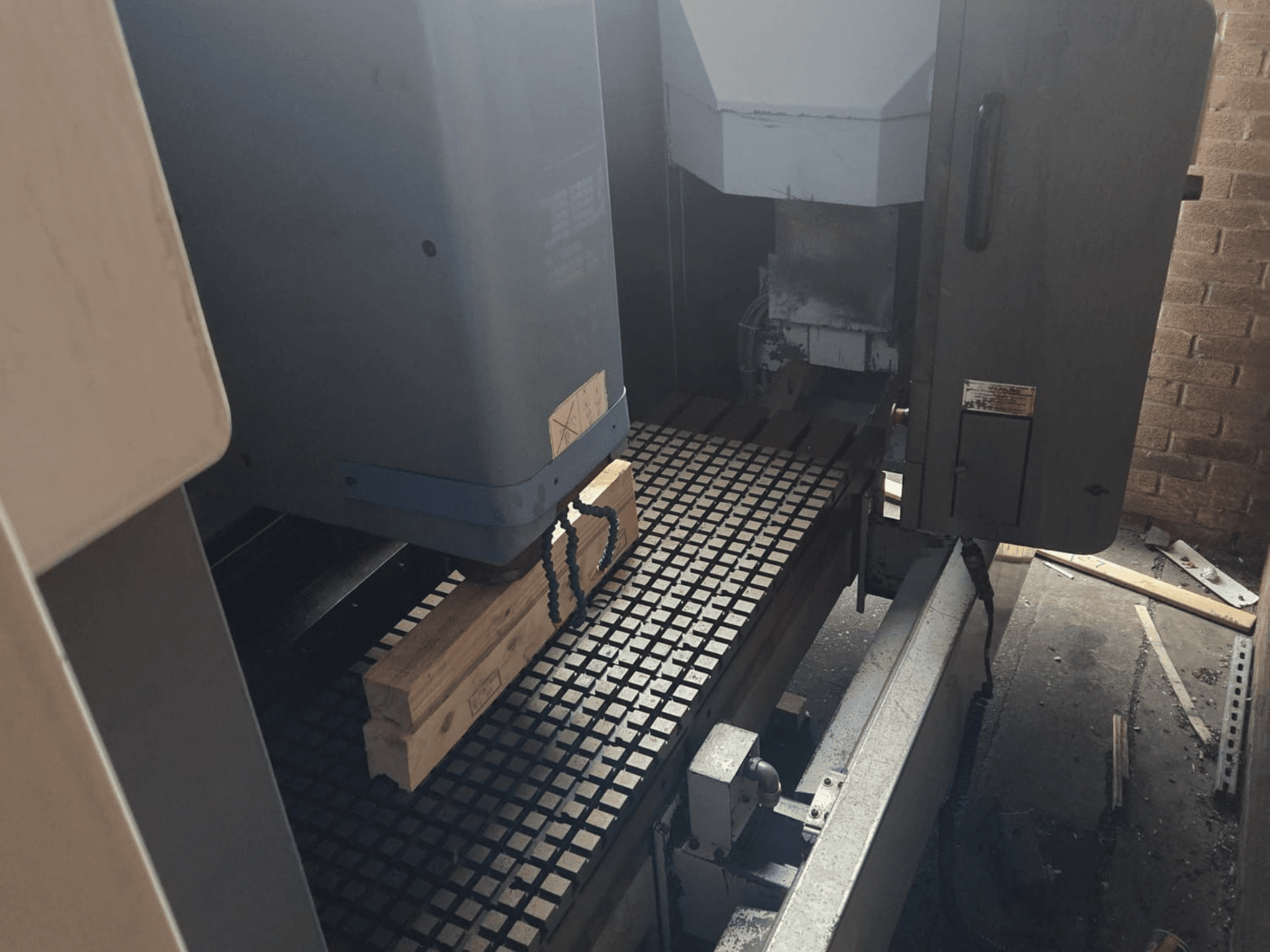 CNC makinesinin önden görünümü, ızgaralı bir masa üzerinde ahşap plakalar, yan tarafta aletler ve kontroller sergileniyor.