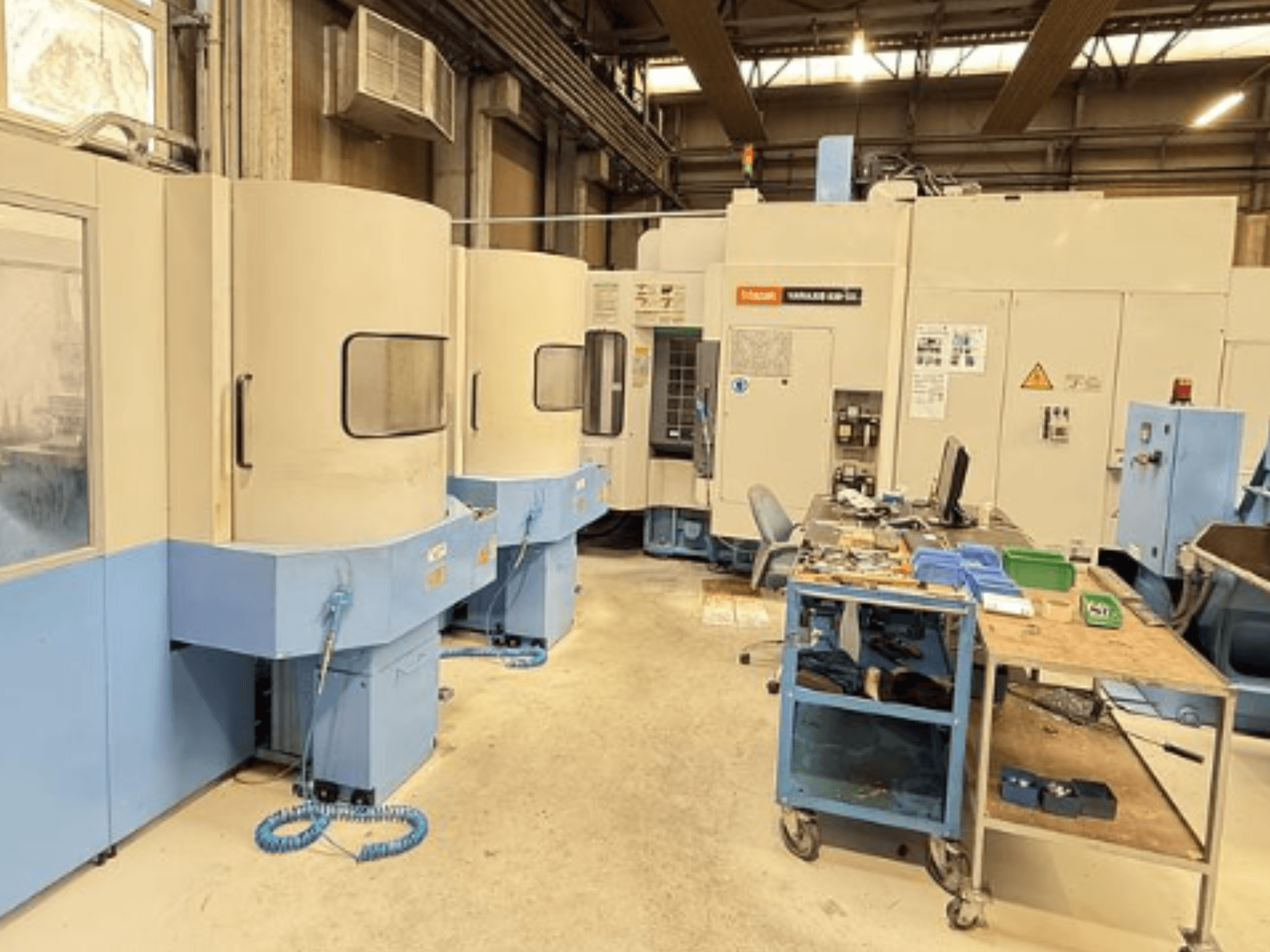 Bir atölyedeki Mazak Variaxis 630-5X dik işleme merkezi, kontrol paneli ve takım depolama alanını gösteren önden görünüm.