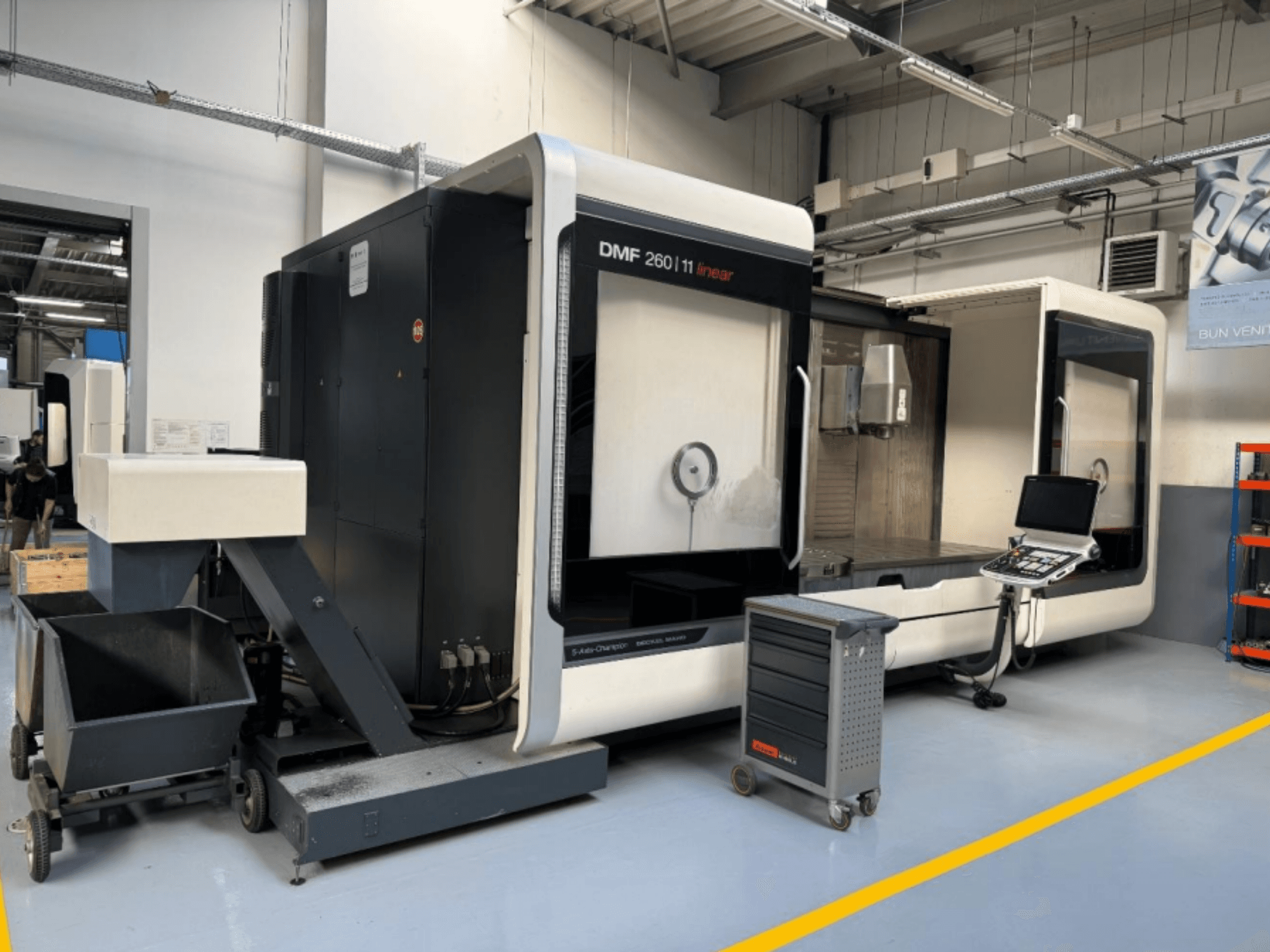 DMG MORI DMF 260 Lineer freze makinesi önden gösterilmiştir, yanında bir takım kontrol paneli ve mobil bir takım arabası bulunmaktadır.