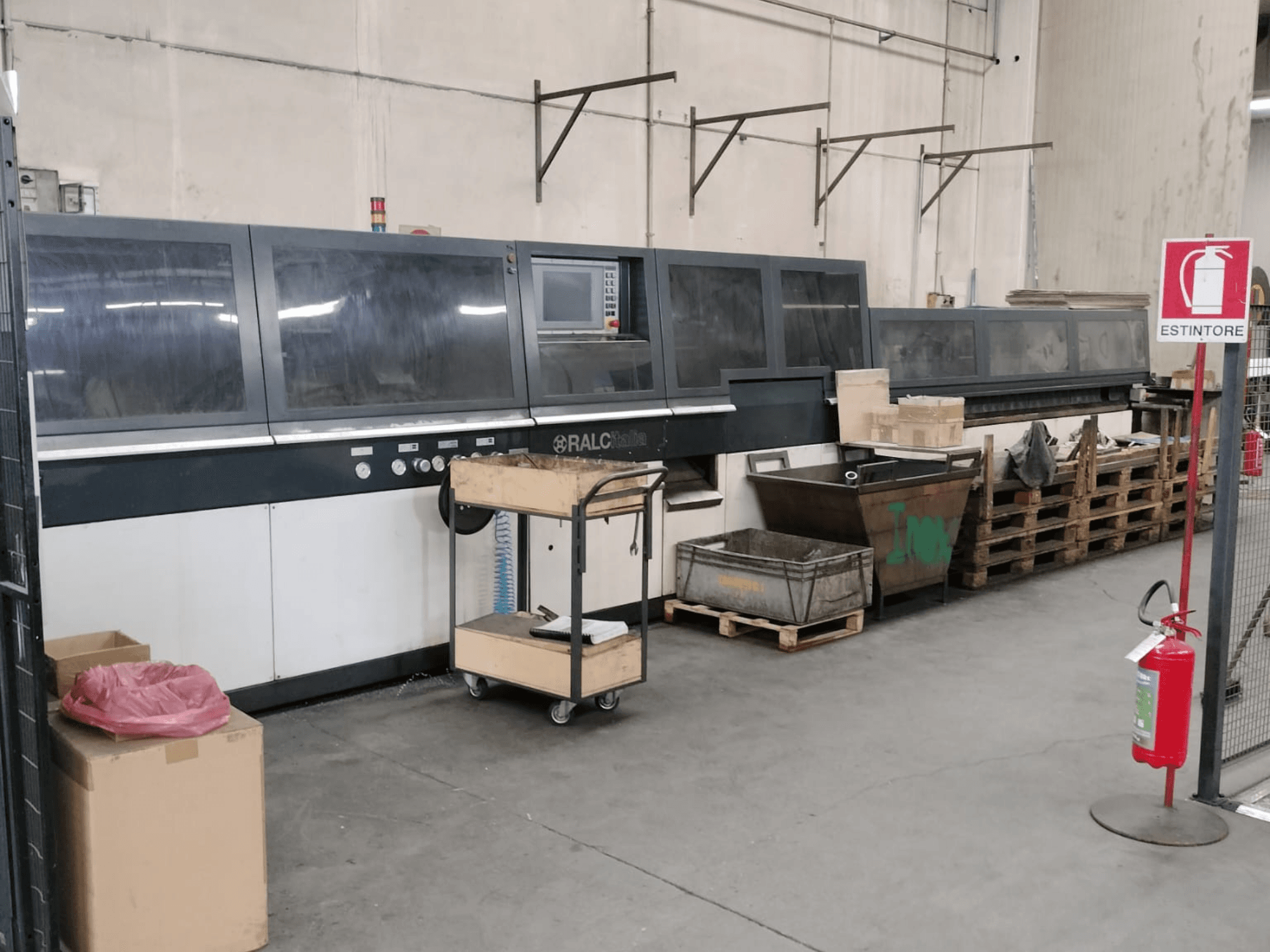 Fabrika ortamında RALC endüstriyel makine, önden görünüm, kontrol paneli görünüyor; ahşap paletler ve yangın söndürücü yakında.