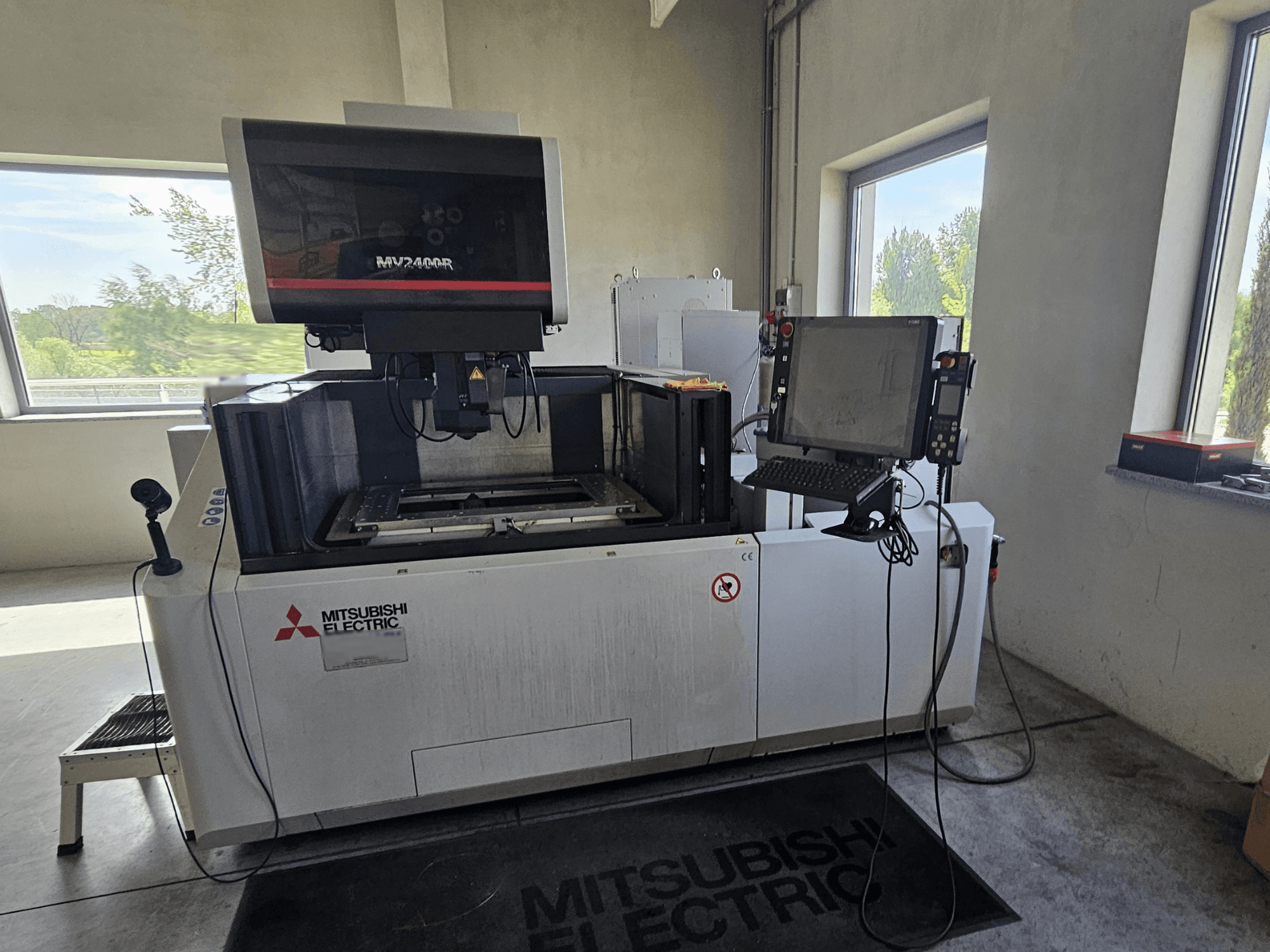 Bir atölyede Mitsubishi MV2400R Tel Erozyon makinesi, dokunmatik ekranlı kontrol paneli ve çalışma alanı.