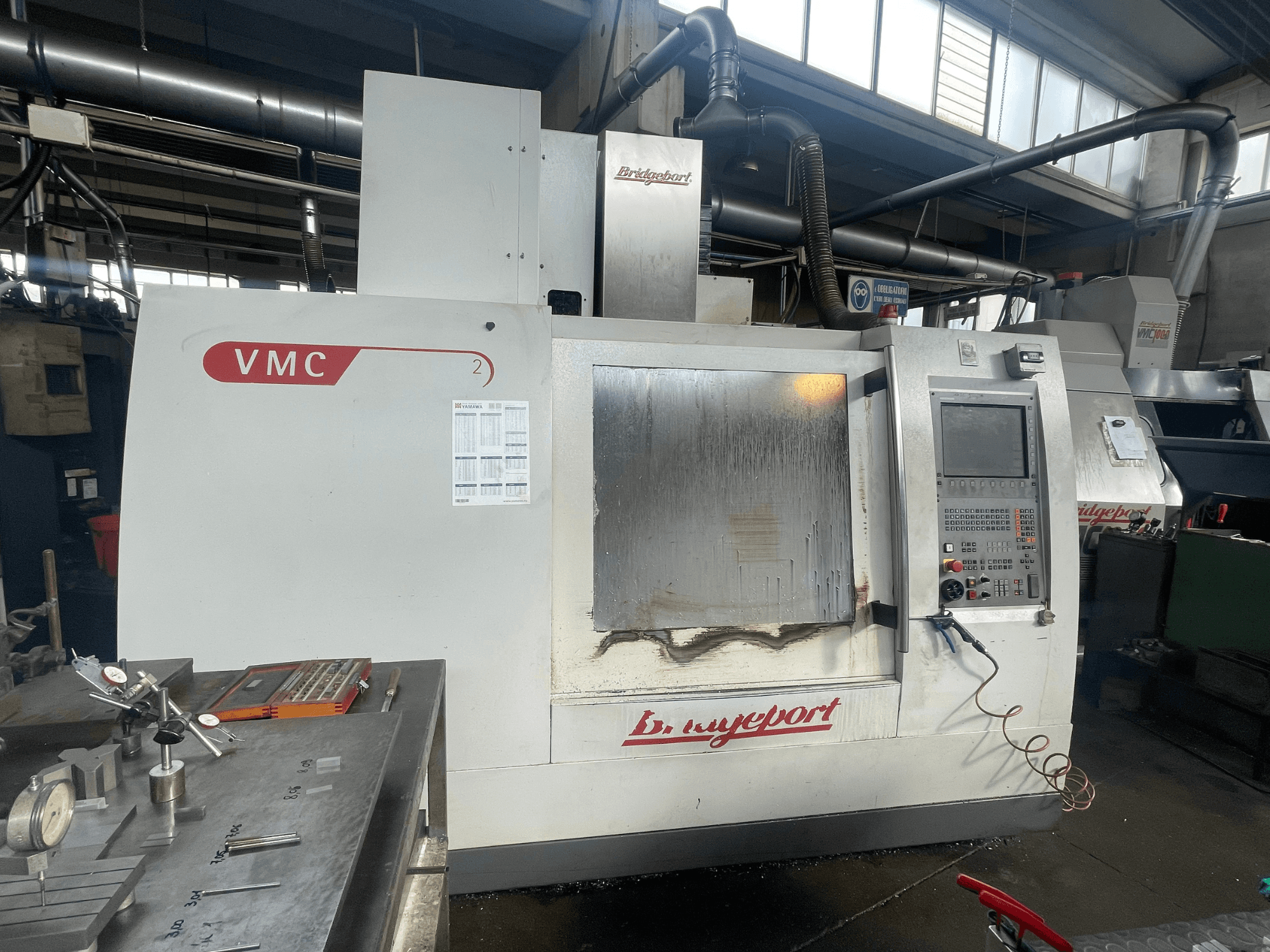 Bir atölyede bulunan, kontrol paneli ve takım tablasına sahip Bridgeport VCM 800-30 dikey işleme merkezi. Ayrıntıları açıkça görülebilen önden görünüm.