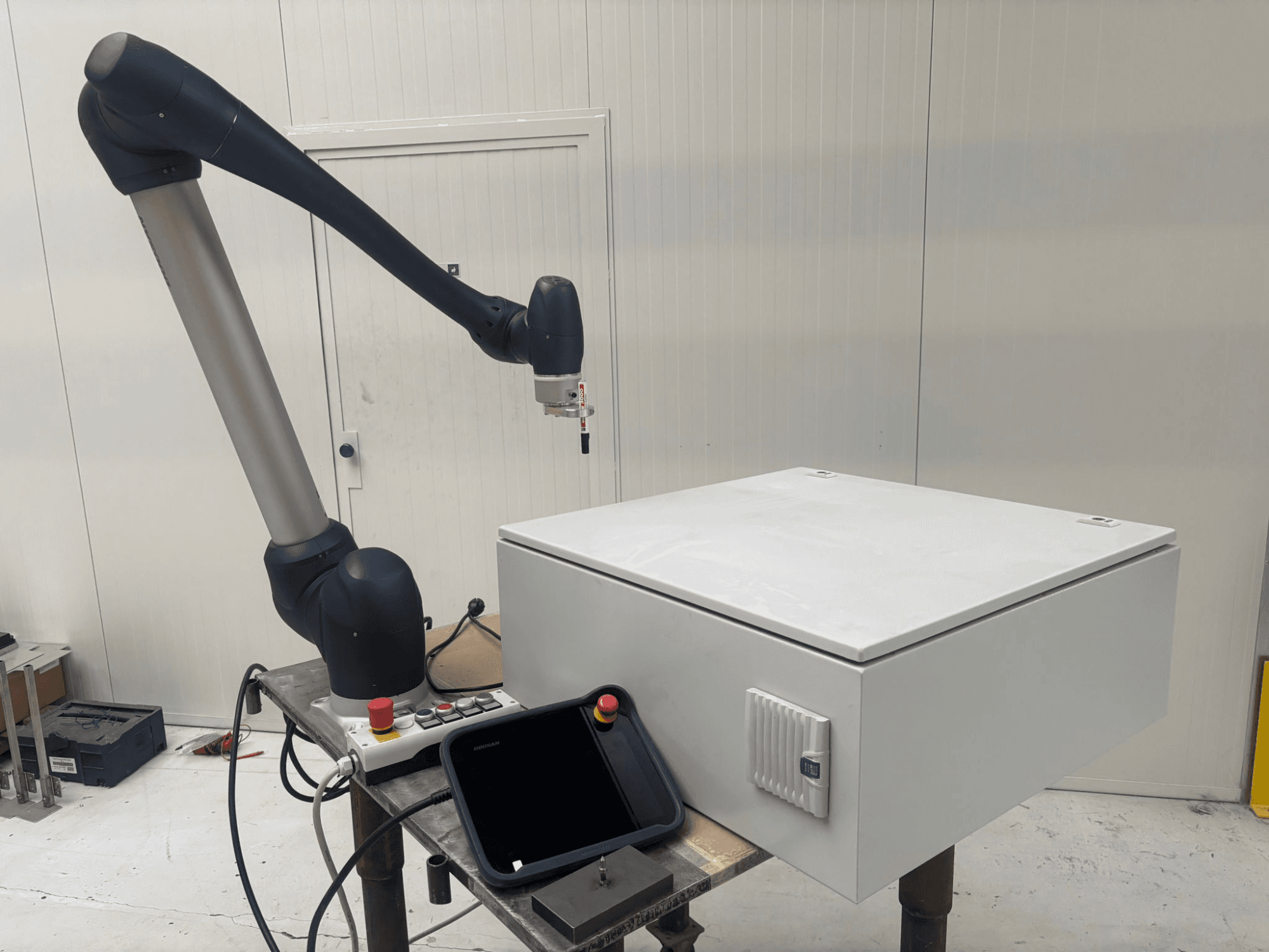 DOOSAN M0617 işbirlikçi robot yan görünümde, robotik kol bir kontrol arayüzünün üzerine uzatılmış ve bir masa üzerinde beyaz bir kutu.
