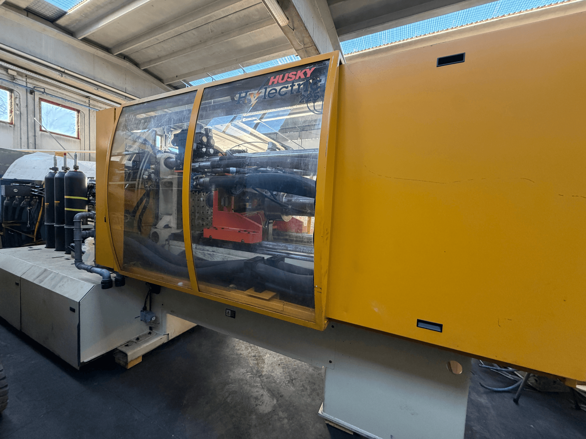 Husky HL225 RS65 elektrikli enjeksiyon kalıplama makinesi, sarı gövde, görünür kontrol paneli ve hidrolik bileşenlerle önden görünüm.