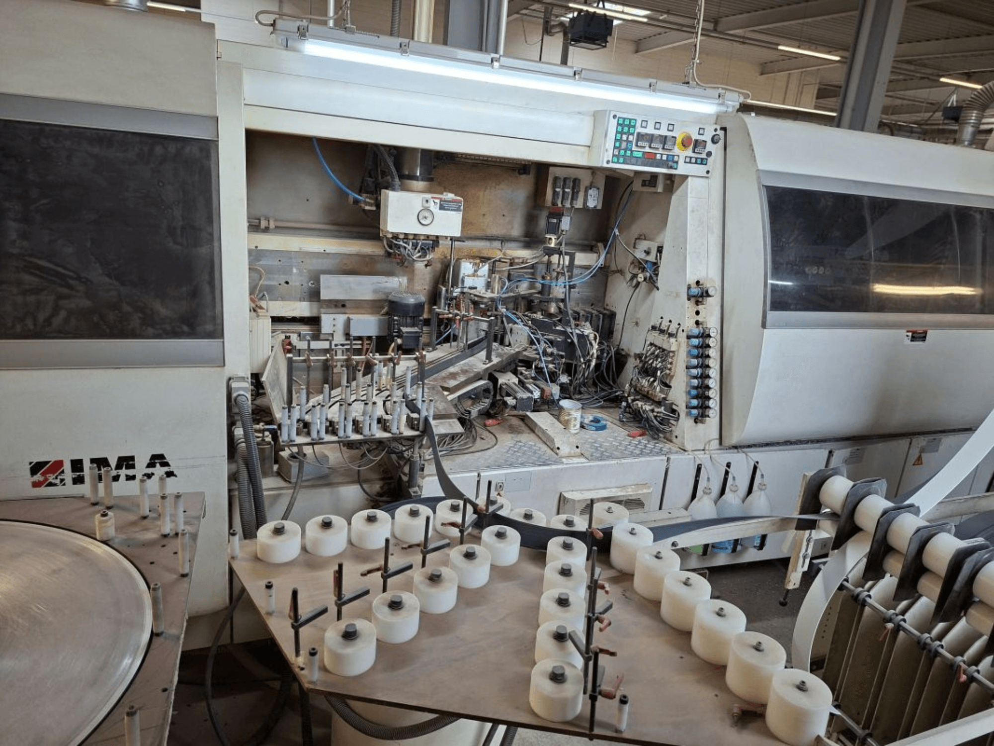 IMA makineleri yandan bakıldığında karmaşık mekanik bileşenleri ve beyaz makaralı yuvarlak bir masayı sergiliyor.