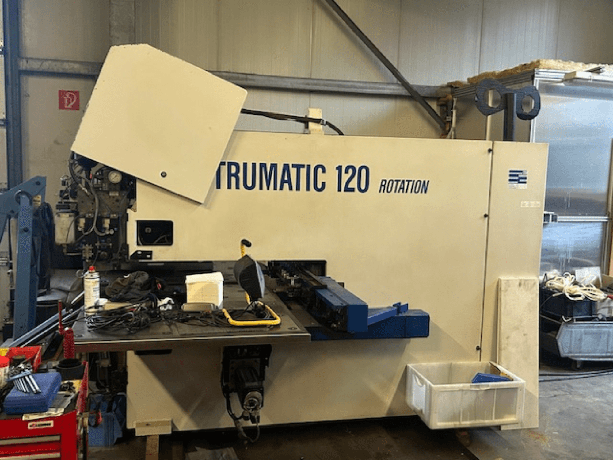 TRUMPF Trumatic 120R CNC delme makinesi atölyede, kontrol paneli ve tabla üzerindeki takımları gösteren önden görünüm.